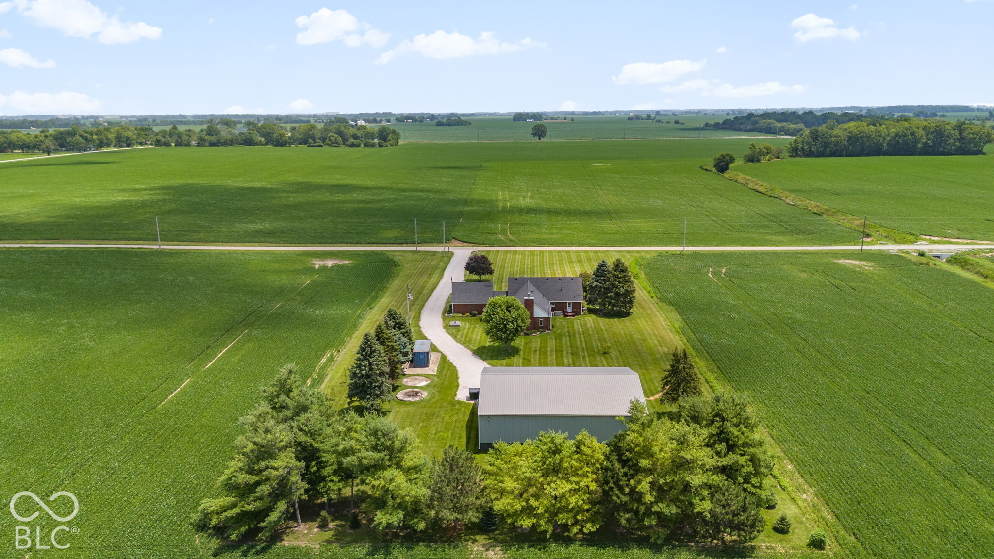 Aerial view of a rural home and barn surrounded by expansive green farmland.