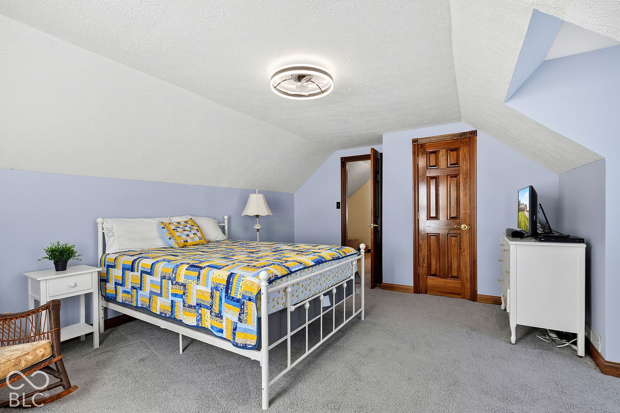 Bedroom with a blue-and-yellow quilt, sloped ceiling, and warm wood doors.
