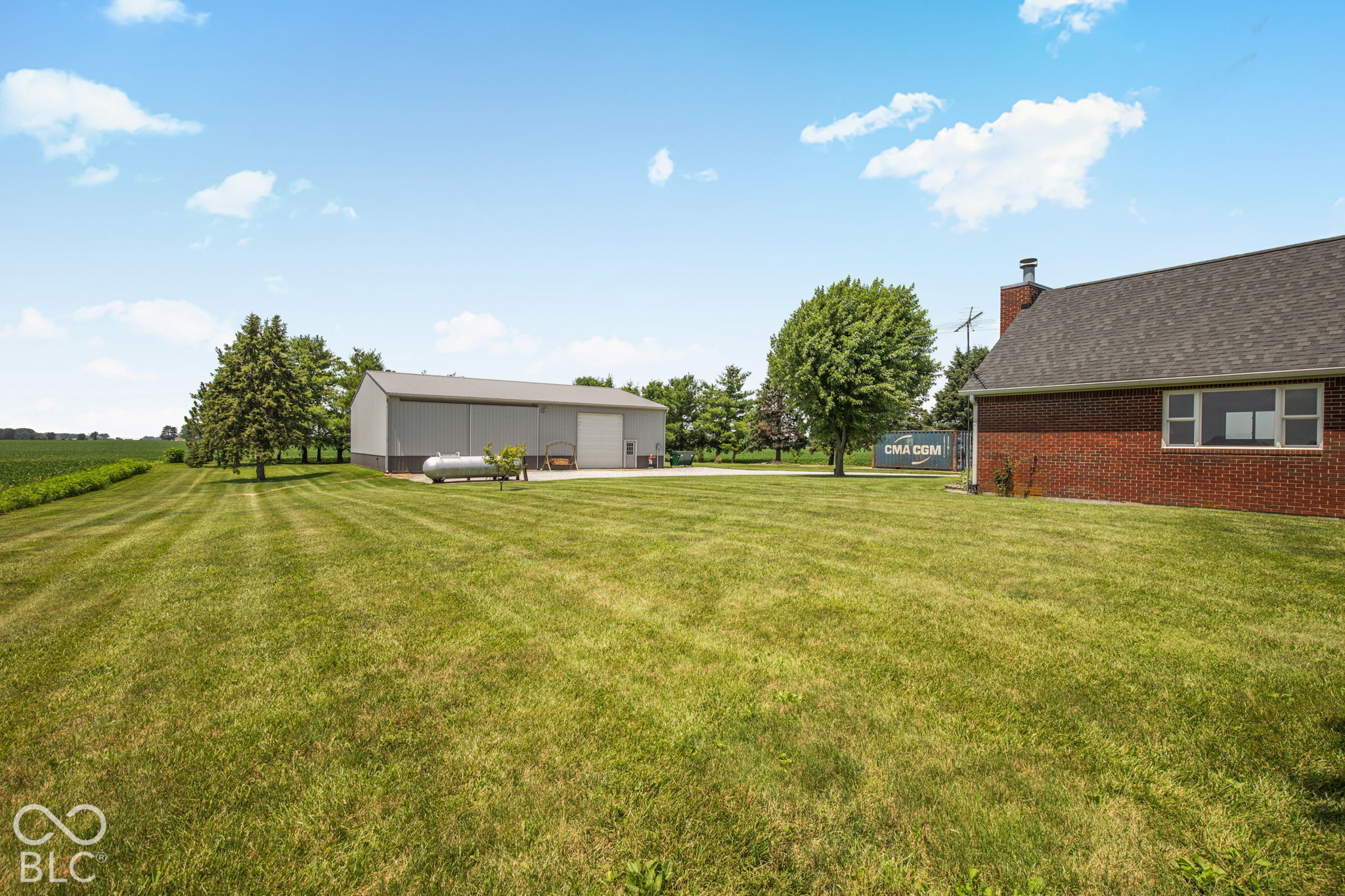 Rural property with a broad mowed lawn, brick house, and large detached metal outbuilding.
