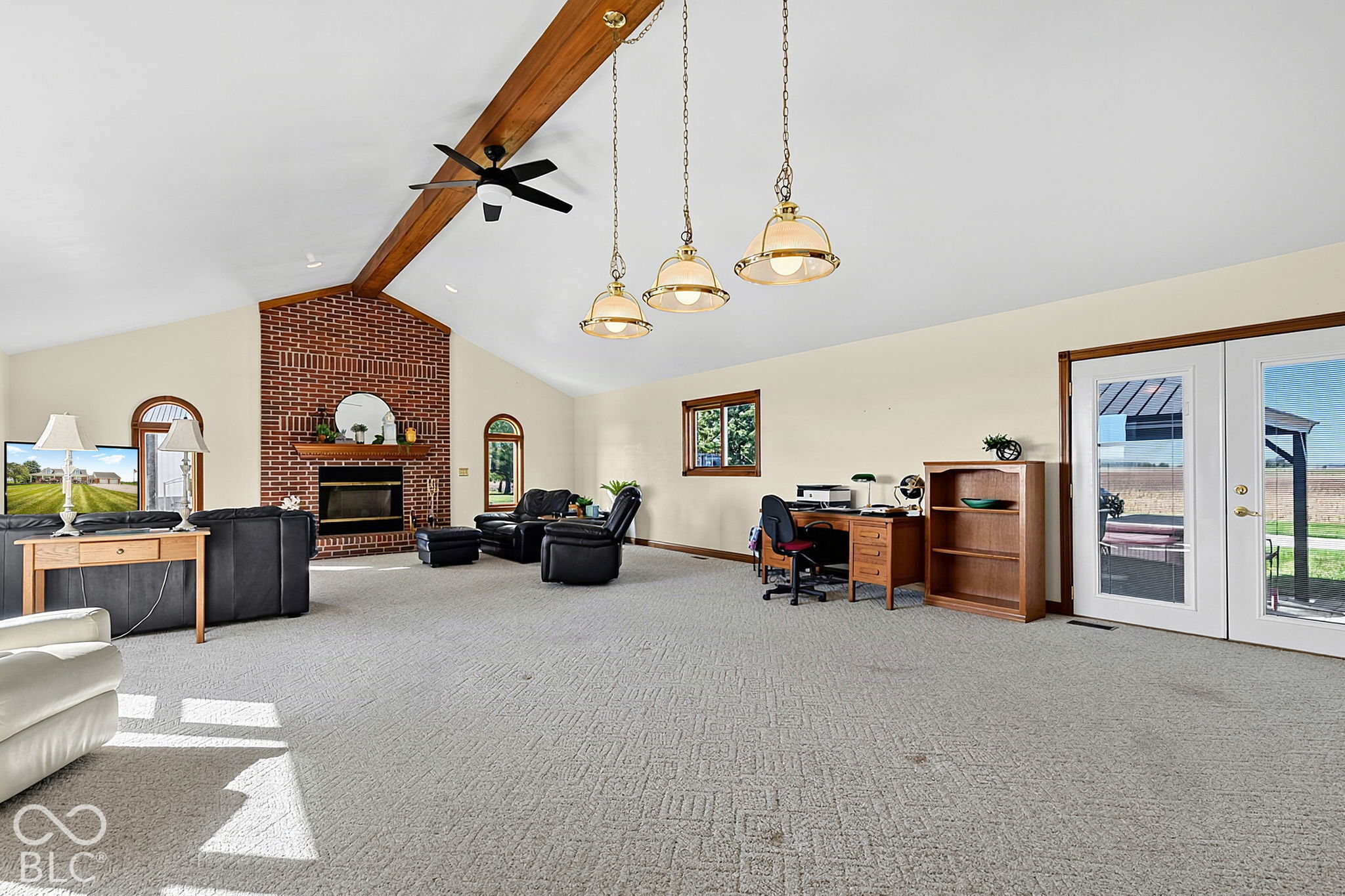 Vaulted living room with exposed wood beam, brick fireplace, leather seating, and French doors to a patio.