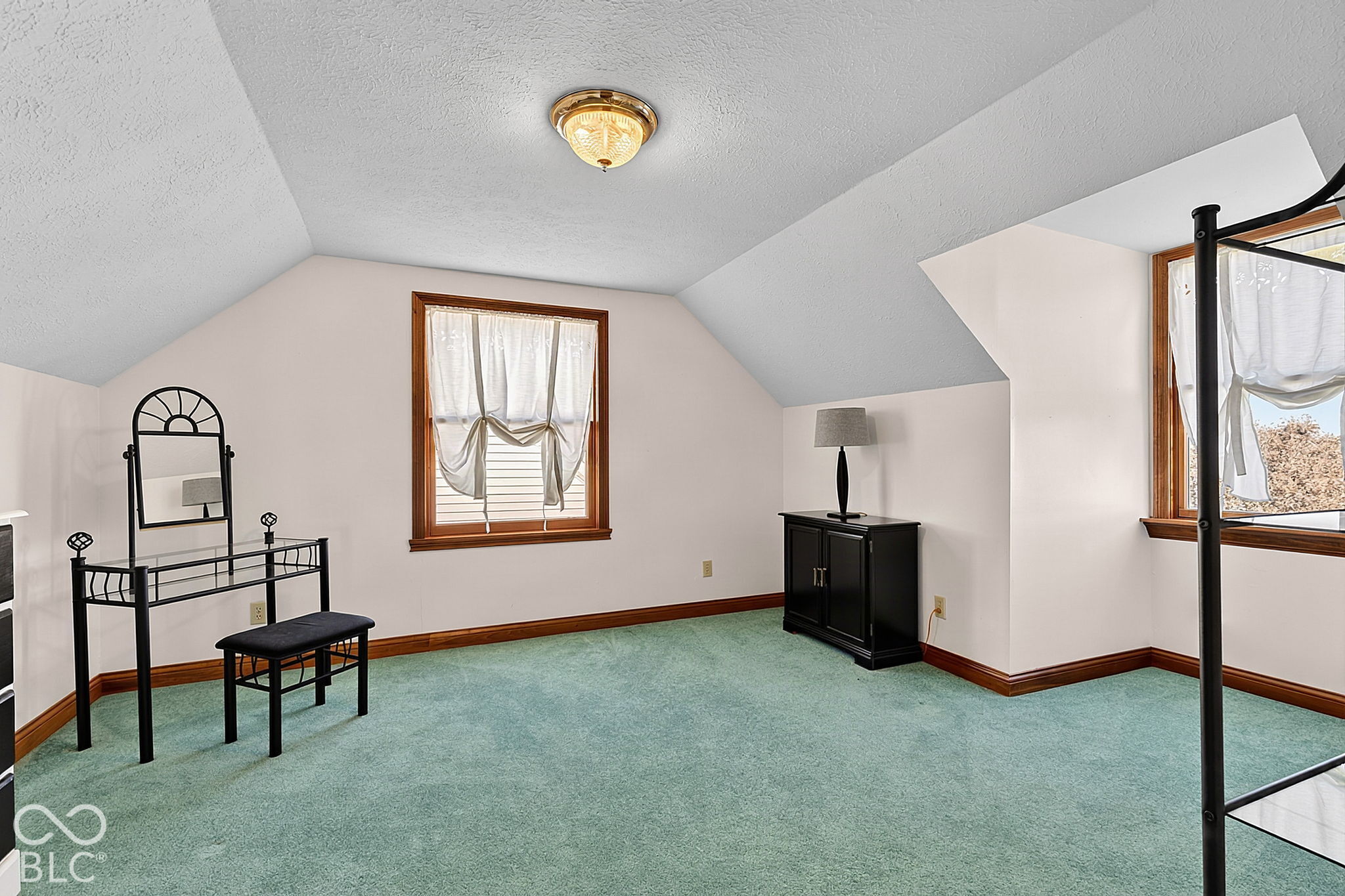 Bedroom with a sloped ceiling, teal carpet, wood-trimmed windows, and a black metal bed frame.