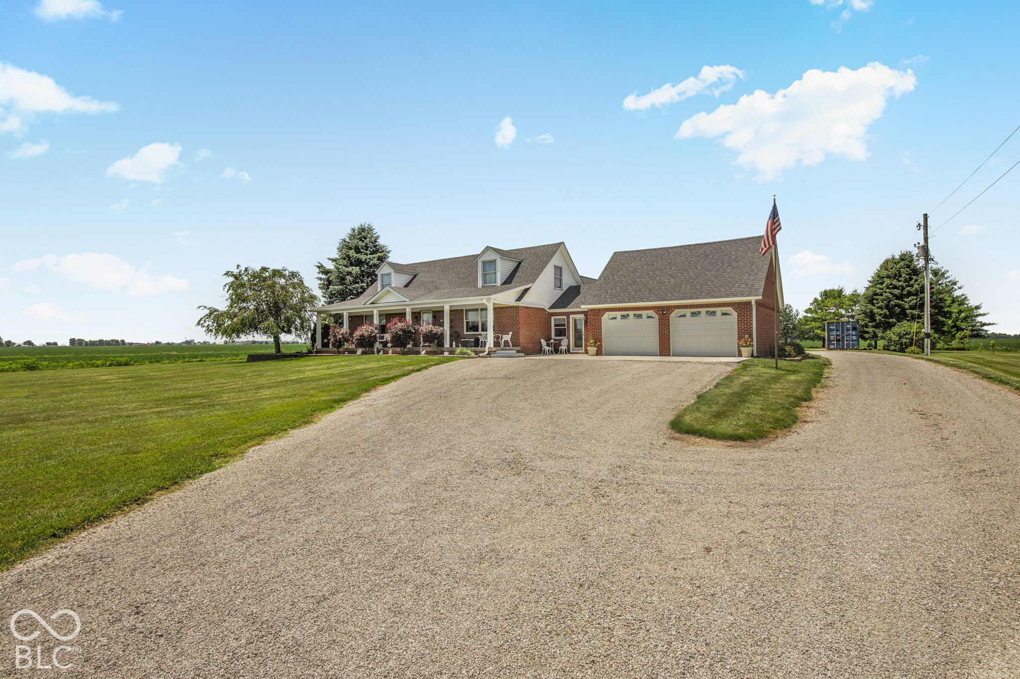 Red-brick country home with a covered porch, attached two-car garage, and wide gravel driveway.