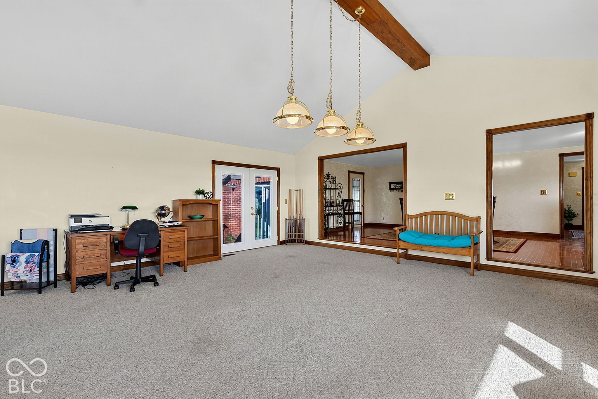 Carpeted living room with an exposed ceiling beam, pendant lights, desk, and wooden bench.