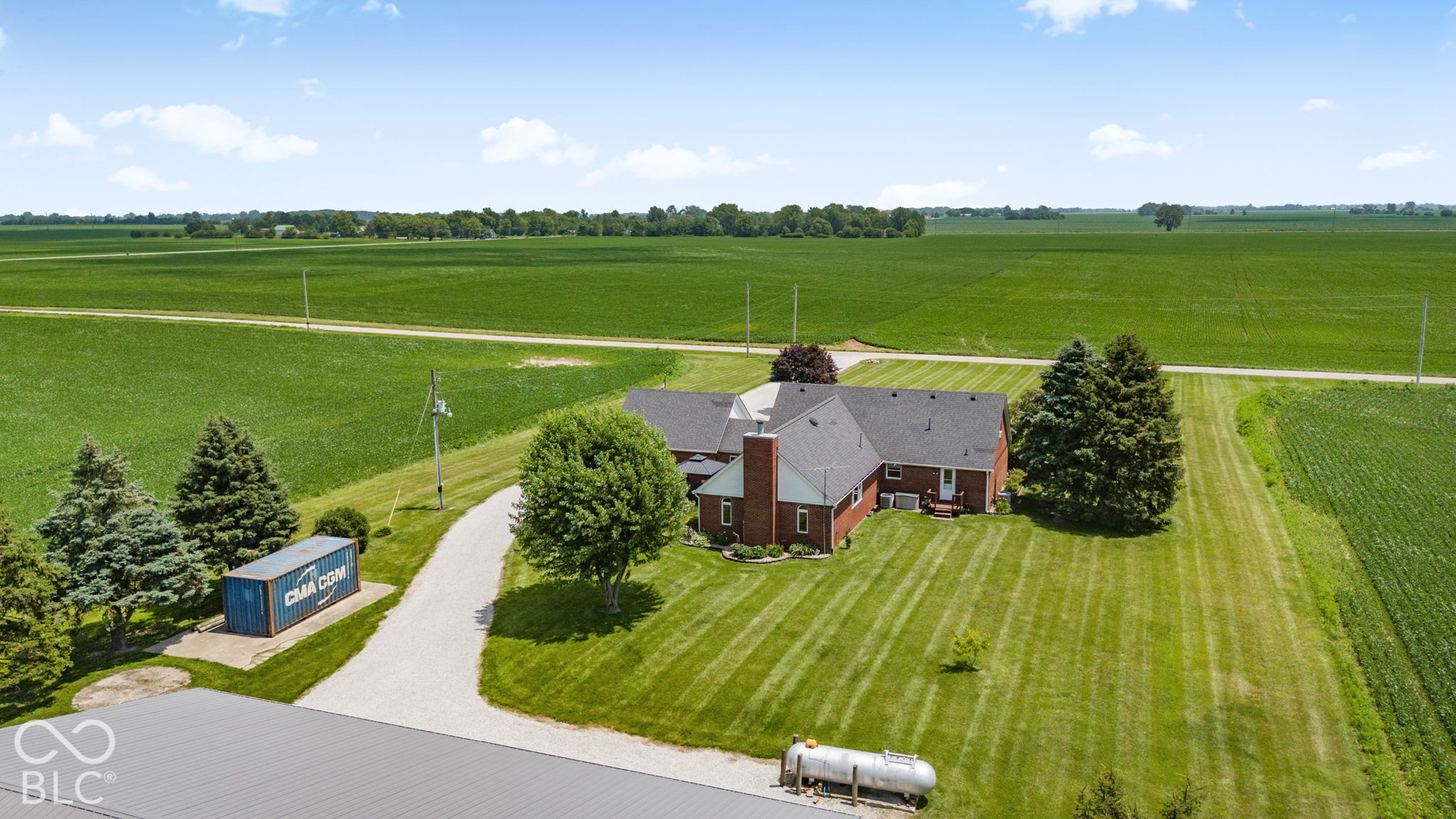 Aerial view of a brick house and mowed grounds surrounded by expansive green fields.