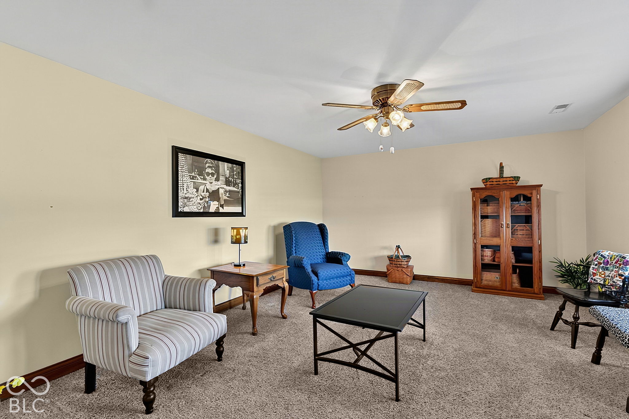 Furnished living room with striped and blue armchairs, a wooden display cabinet, and ceiling fan.