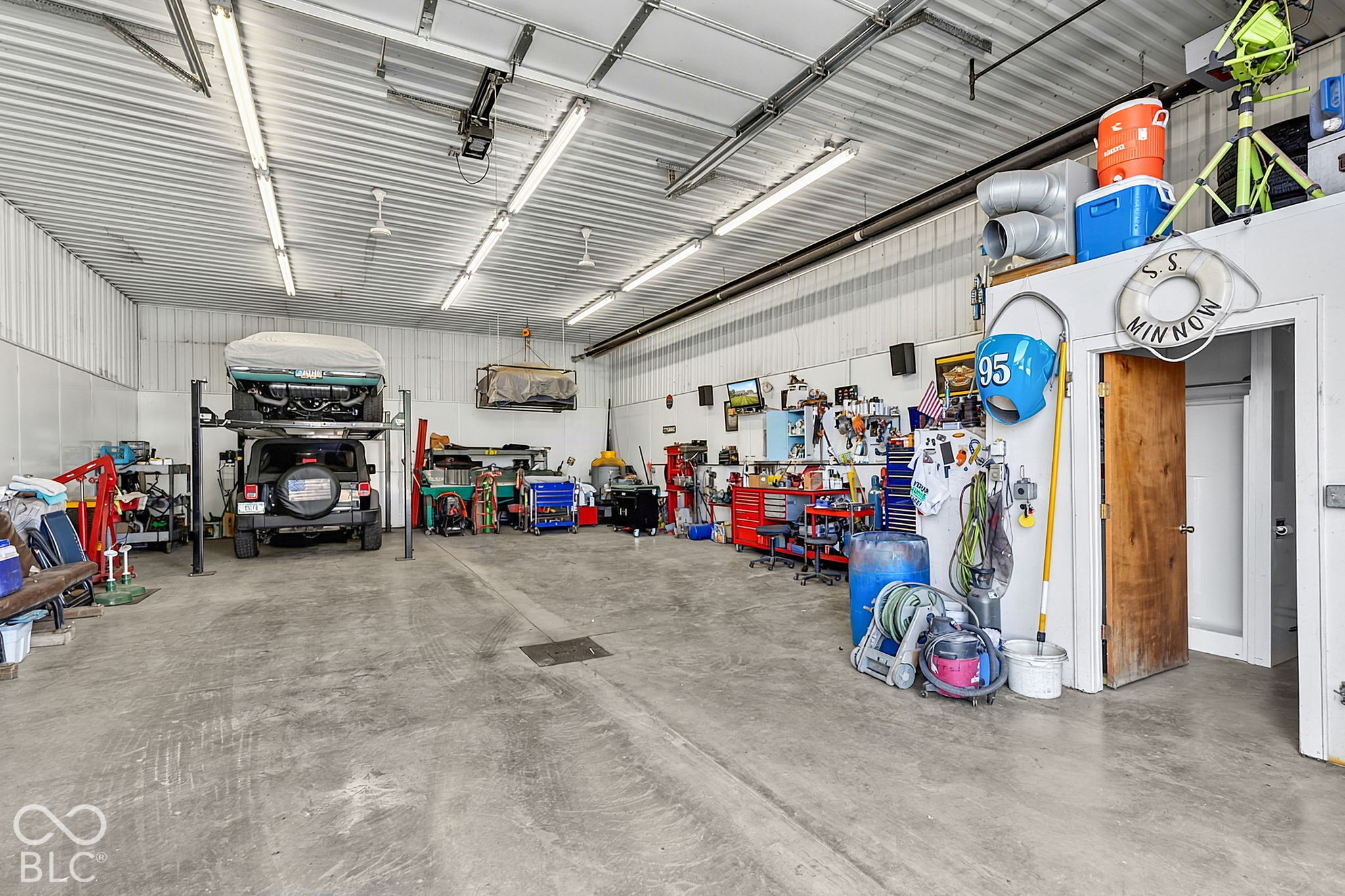Large garage workshop with a vehicle under a raised boat, tool chests, and equipment along the walls.