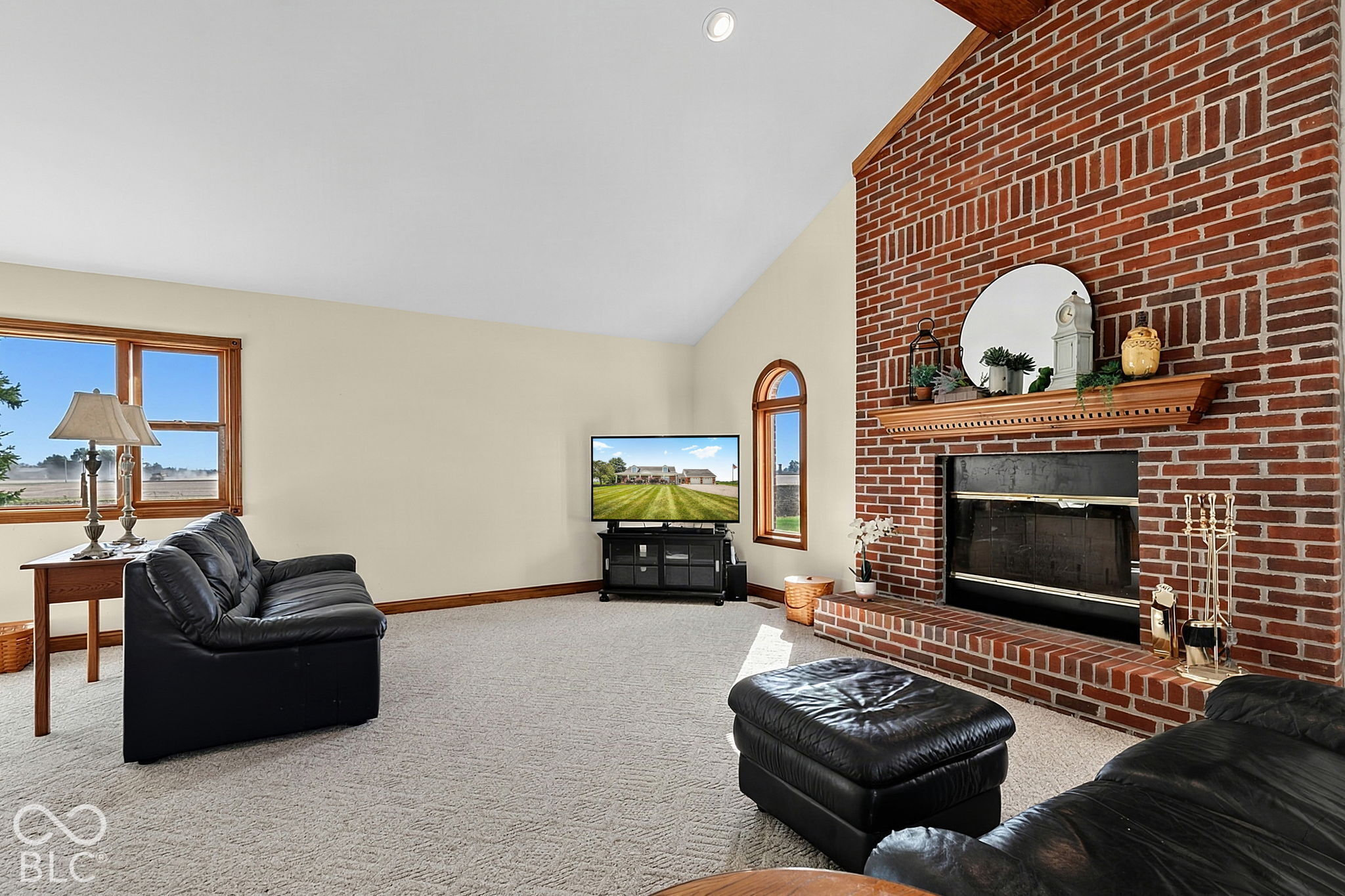 Living room with a brick fireplace, black leather seating, and large wood-trimmed windows.