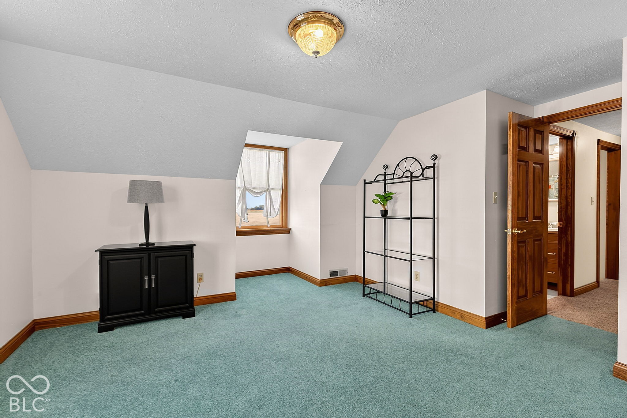 Upstairs room with a sloped ceiling, teal carpet, a small window, and sparse furnishings.