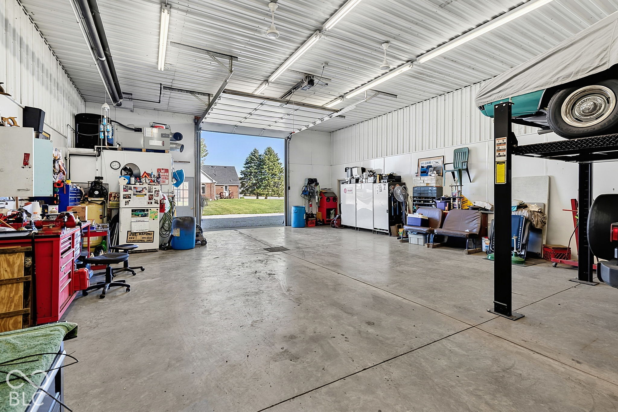 Spacious workshop garage with an open overhead door, tool storage, and a classic car on a lift.