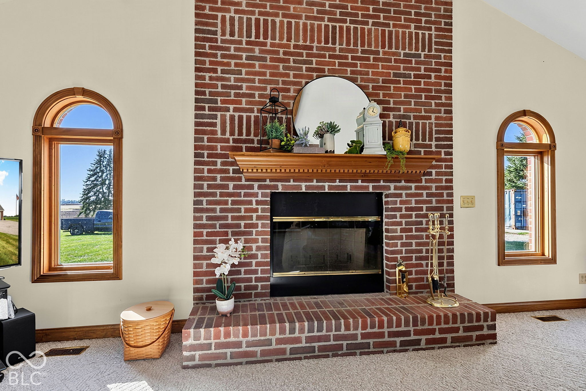 Living room fireplace with a red brick surround, raised hearth, wooden mantel, and arched windows.