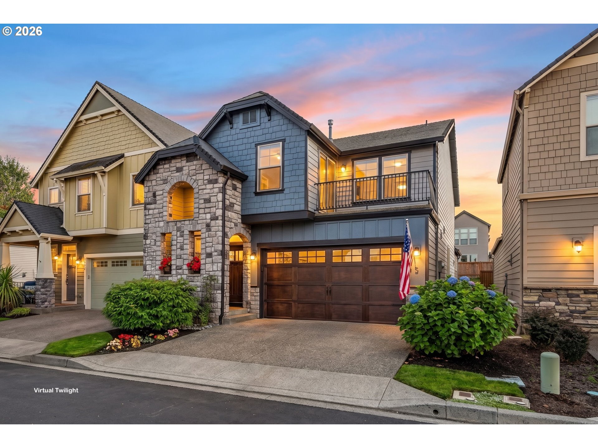Blue two-story house with a stone entry, balcony, and landscaped front yard at dusk.