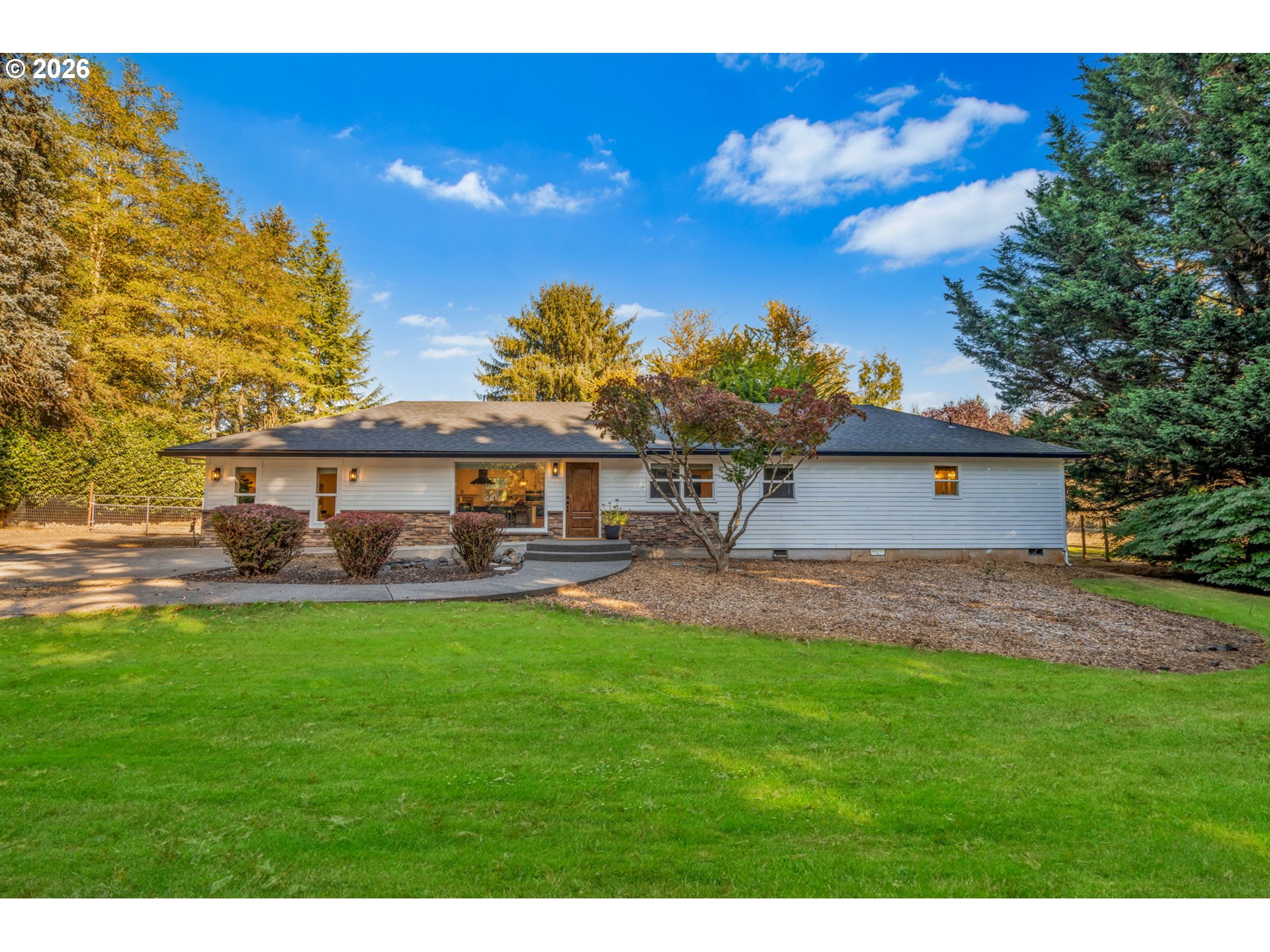 White ranch-style home with stone accents and a broad green lawn, framed by autumn trees.