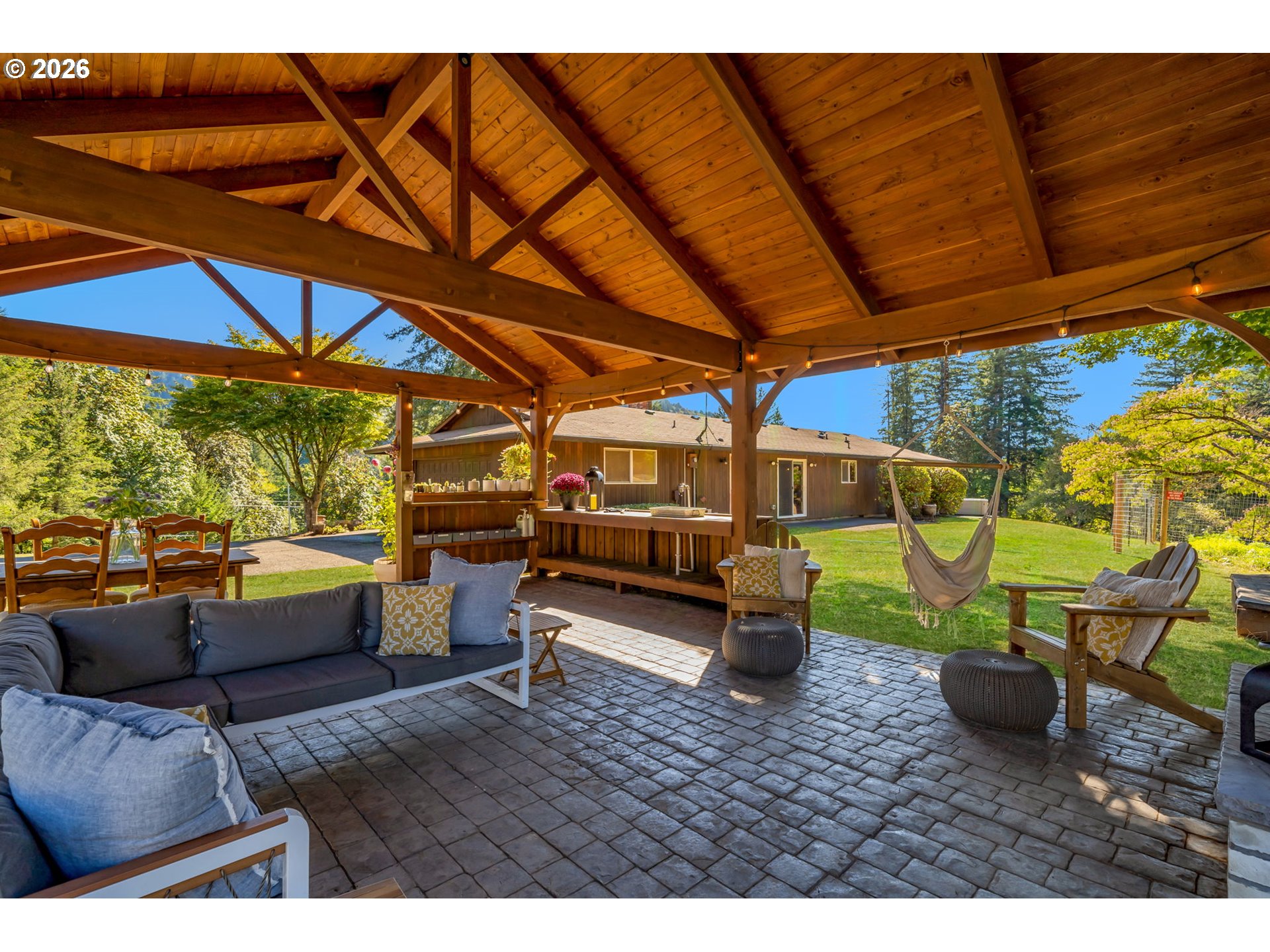 Covered timber patio with lounge seating, stone pavers, and a hammock overlooking the lawn.
