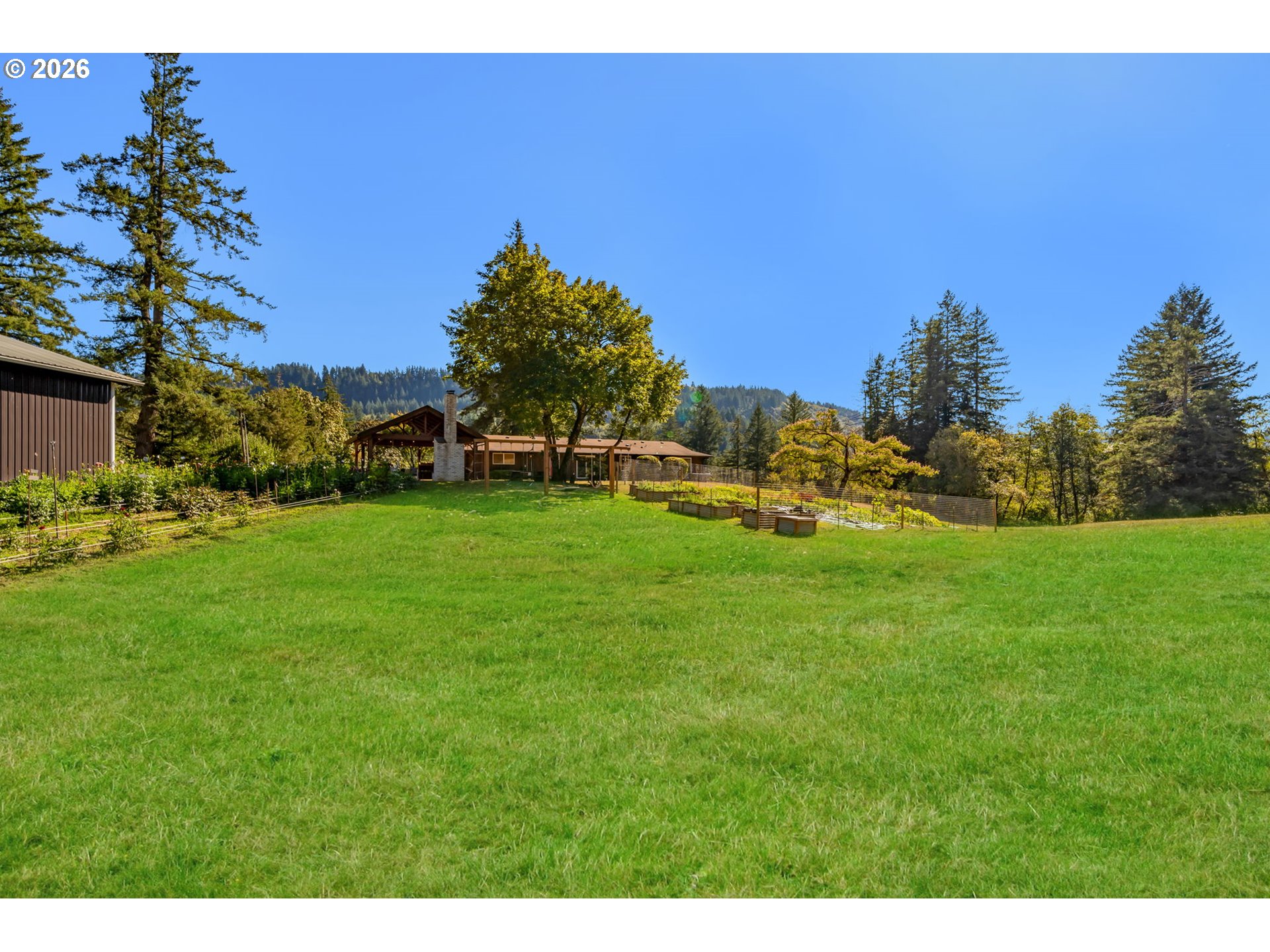 Expansive grassy yard with a wooded-ridge backdrop, raised garden beds, and a low-profile home.