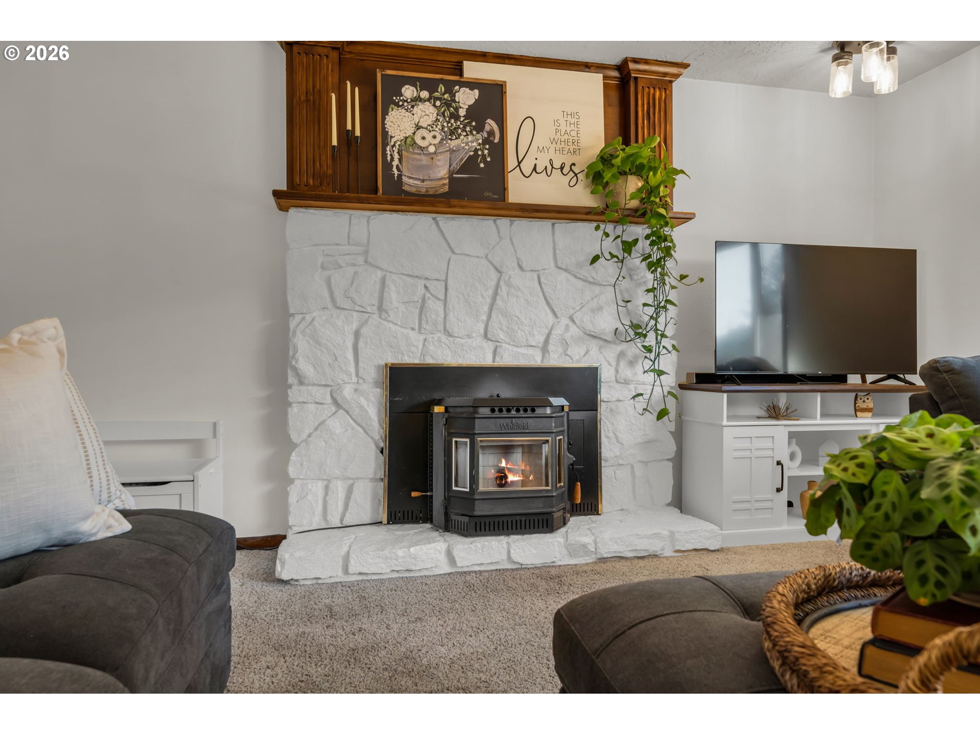 Living room with a lit wood stove in a white stone fireplace and a dark wood mantel.