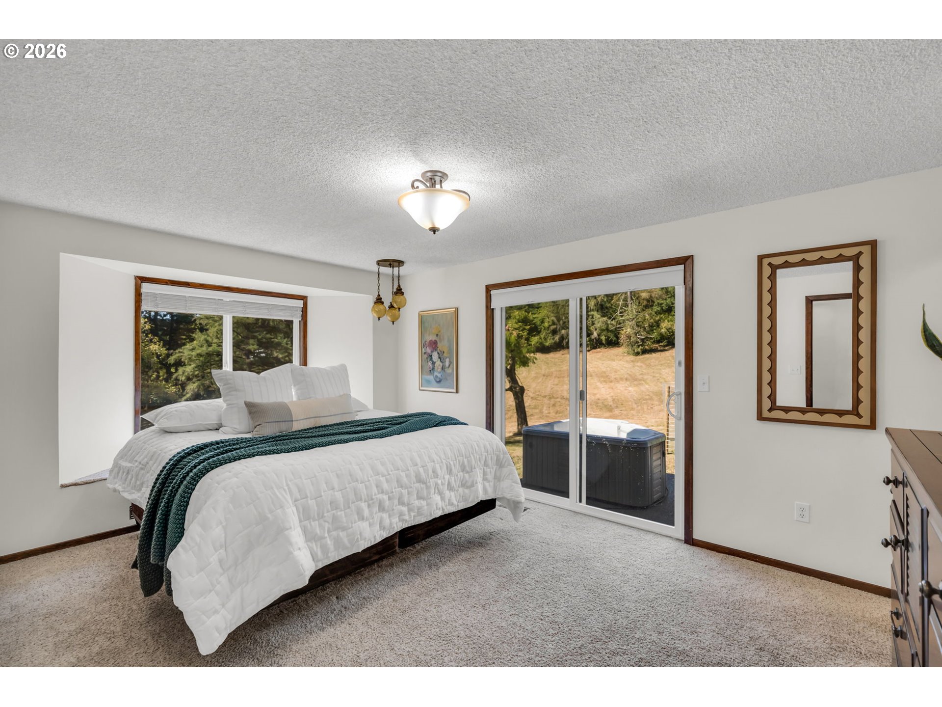 Bedroom with a white bed and teal throw, sliding glass door, and outdoor hot tub.