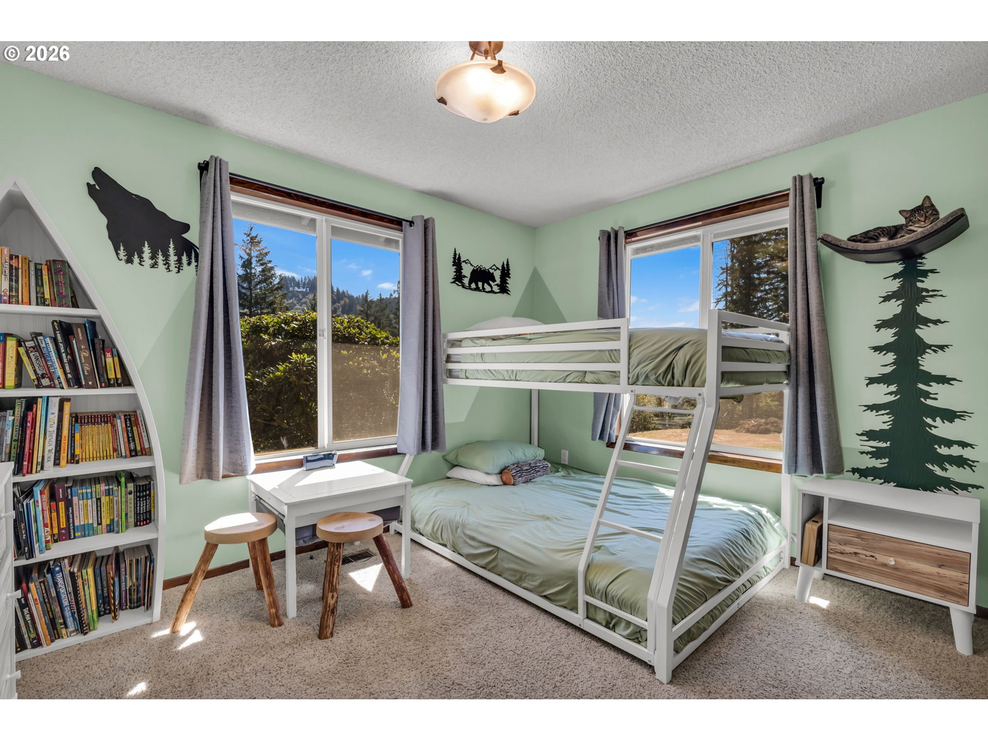 Bedroom with a white bunk bed, sage-green bedding, and large windows overlooking trees.