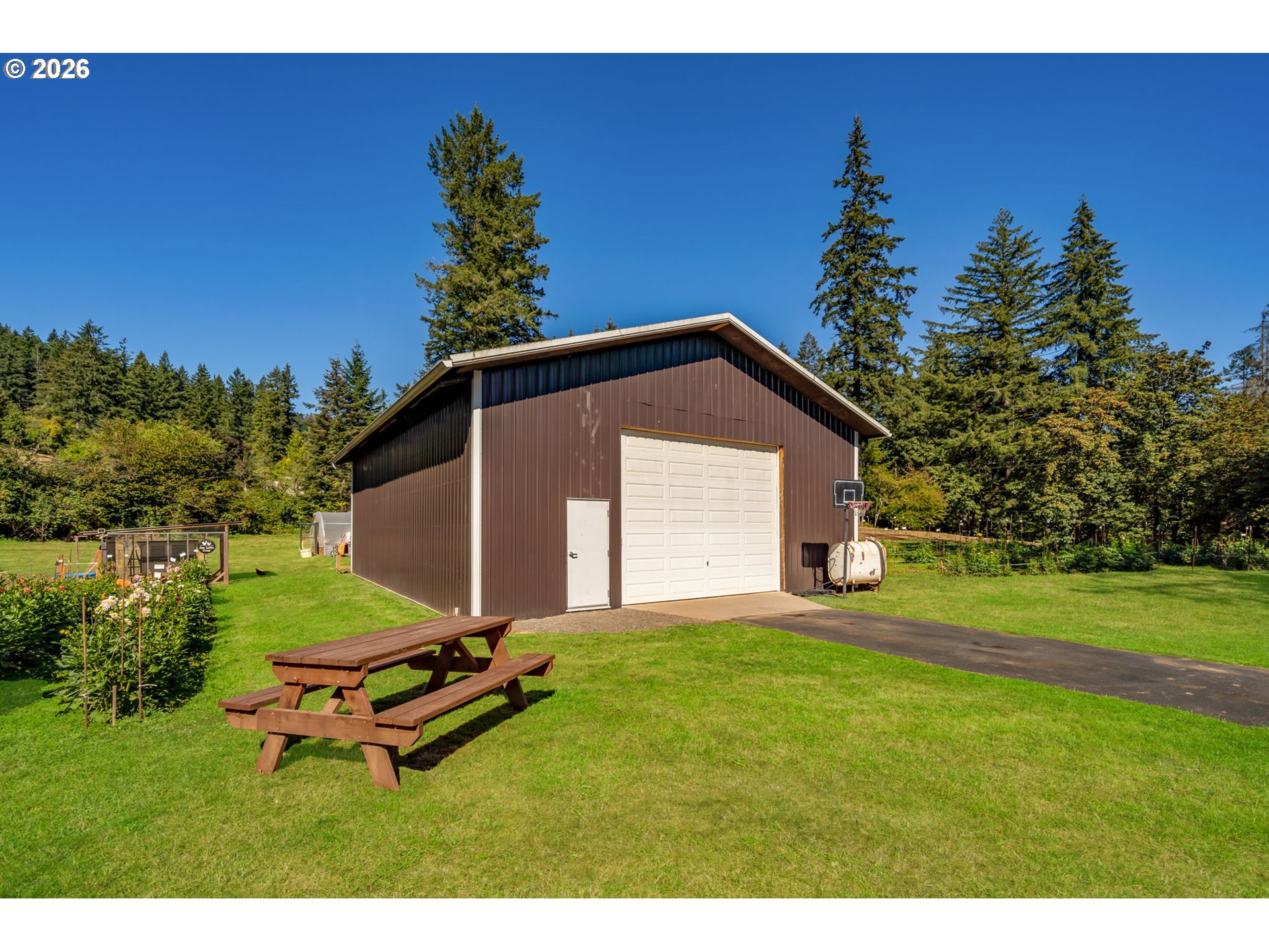 Large brown detached garage with a white overhead door, lawn, driveway, and picnic table.
