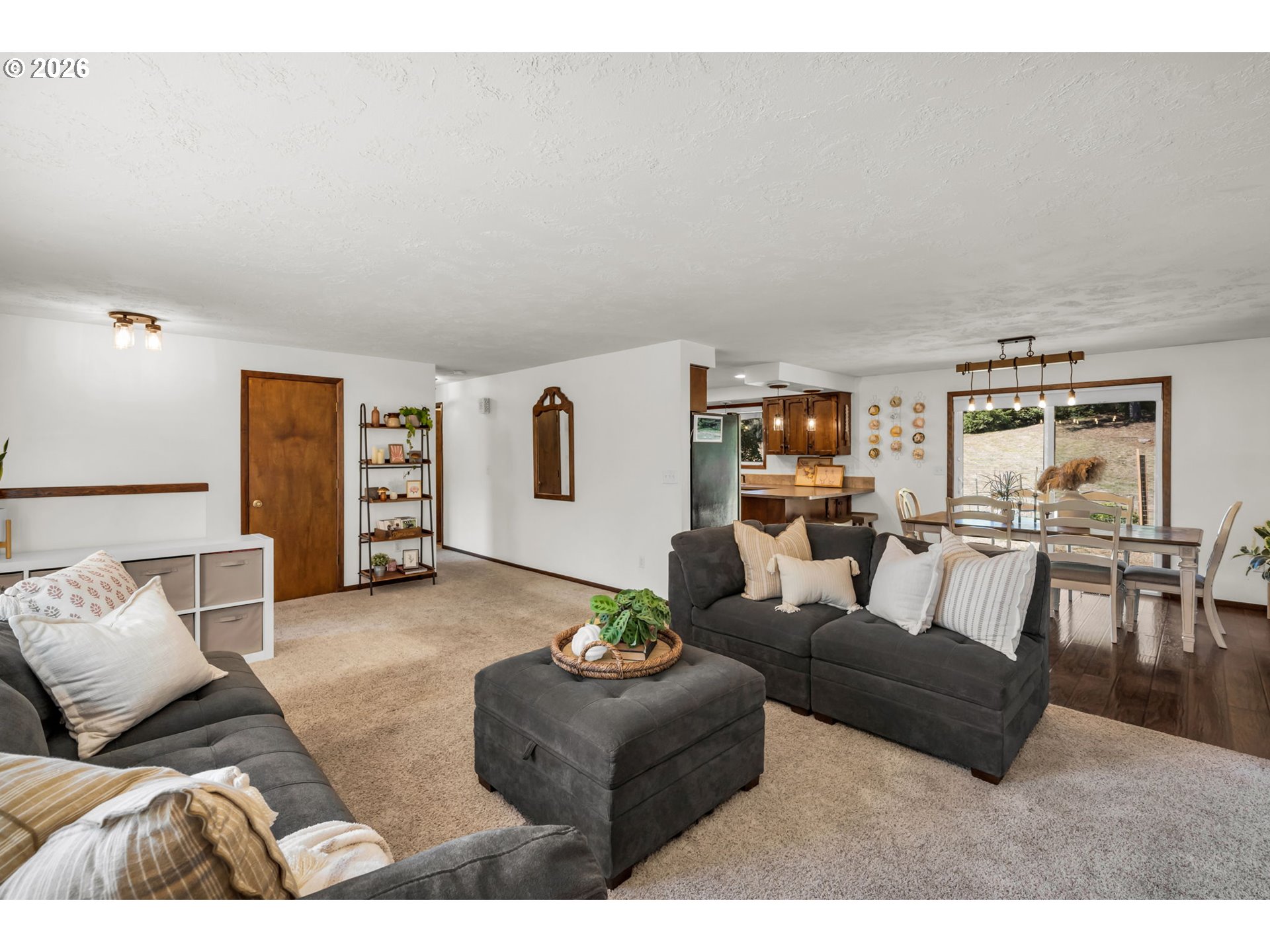 Open-plan living room with gray sectional sofas, carpeted seating area, and dining space beside large glass doors.