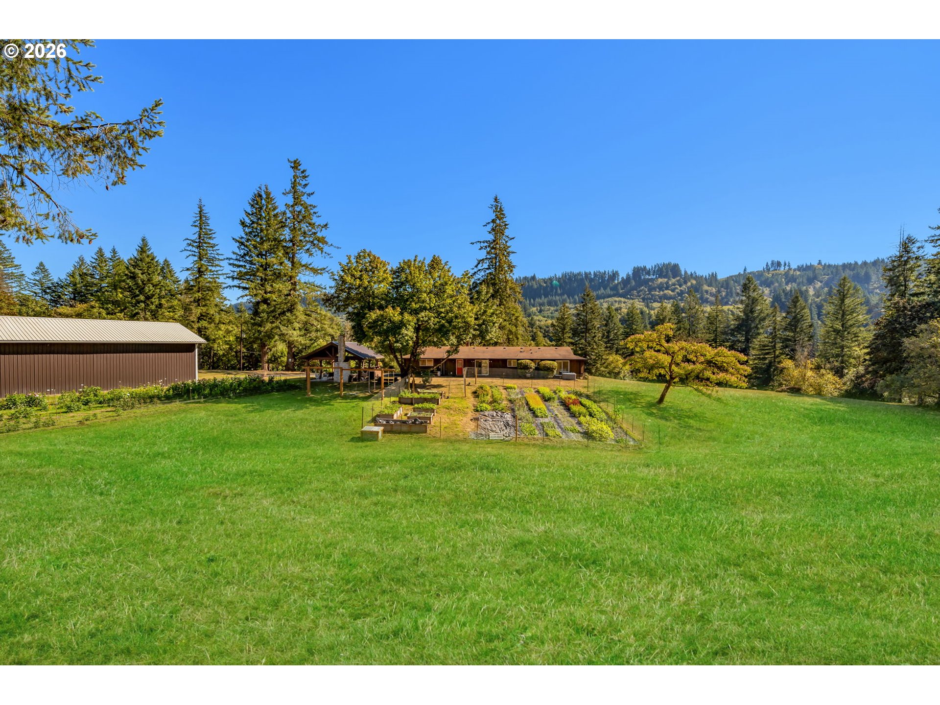 Home and vegetable garden beyond a broad lawn, backed by wooded hills.