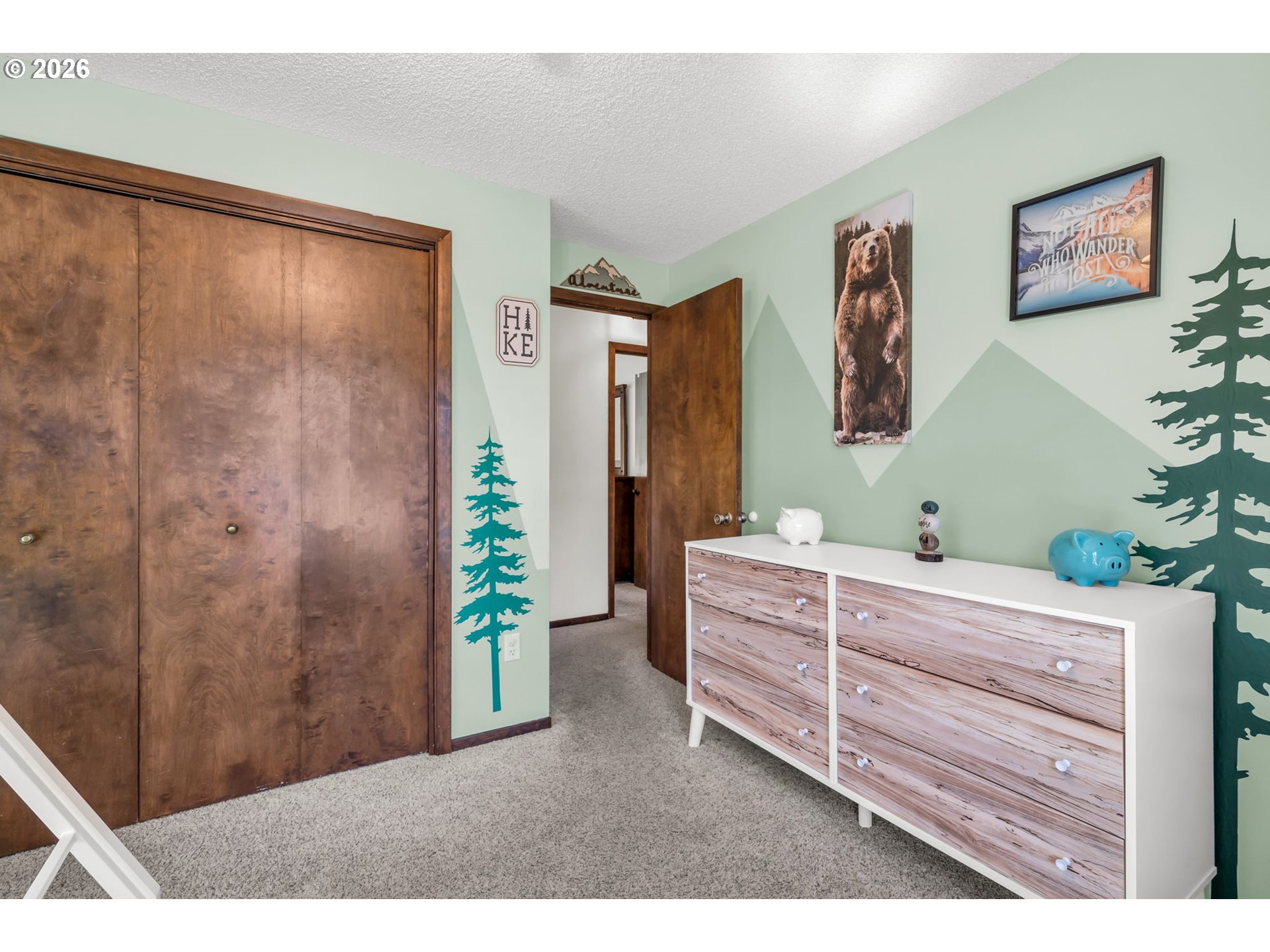 Bedroom with wooden sliding closet doors, a white wood-look dresser, and forest-themed wall decor.