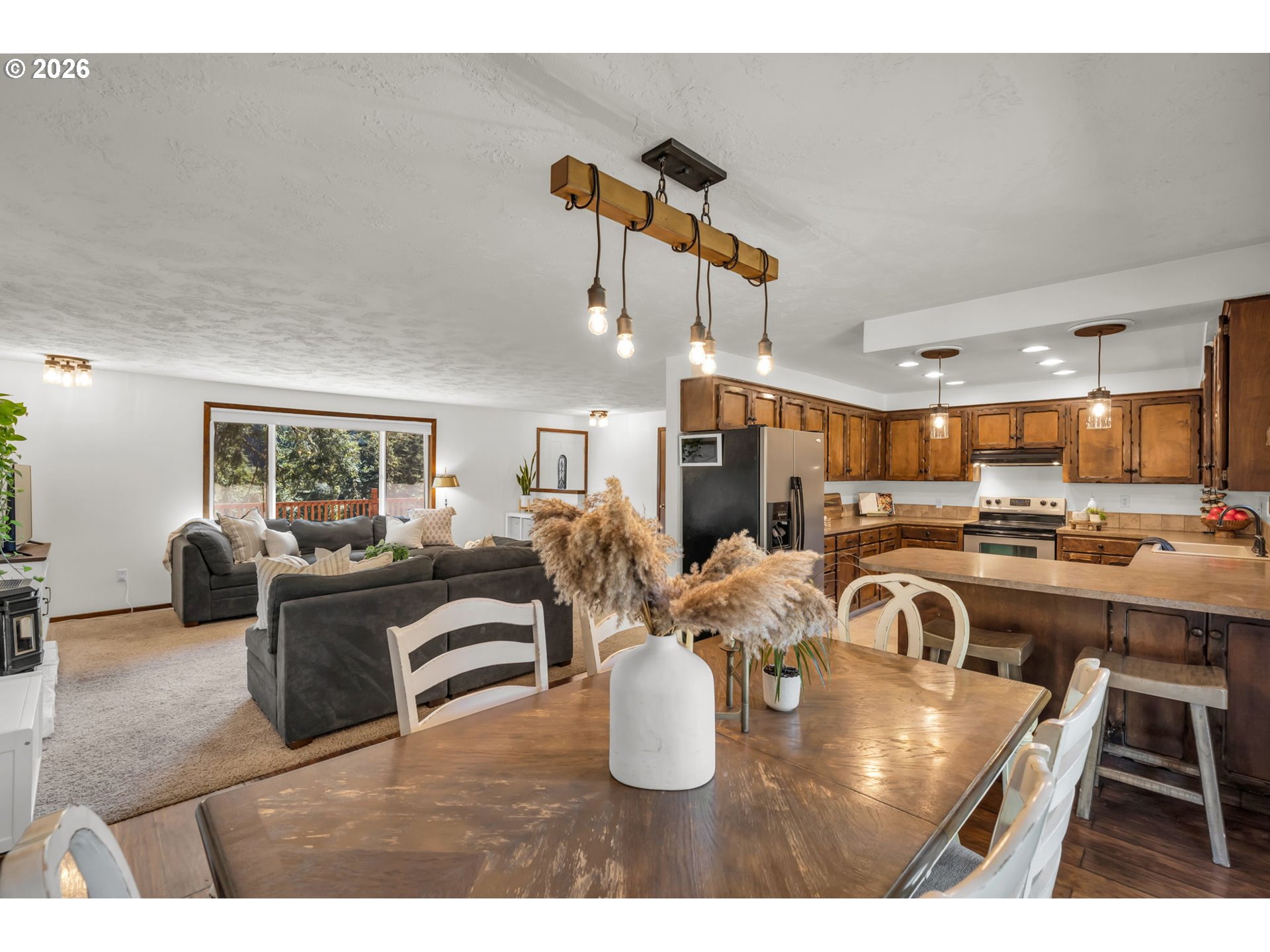 Open-plan kitchen and living room with warm wood cabinets, a dining table, and gray sectional.