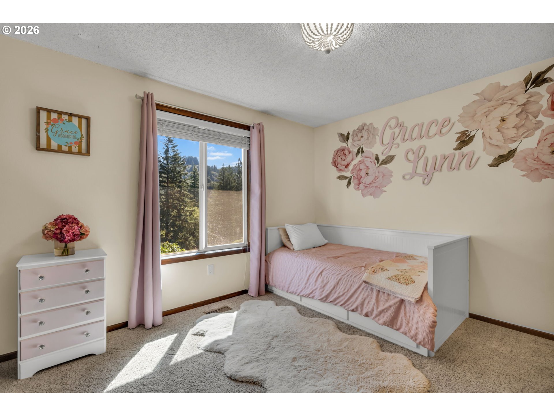 Pink-themed bedroom with a white daybed, floral wall decals, and a sunlit window.