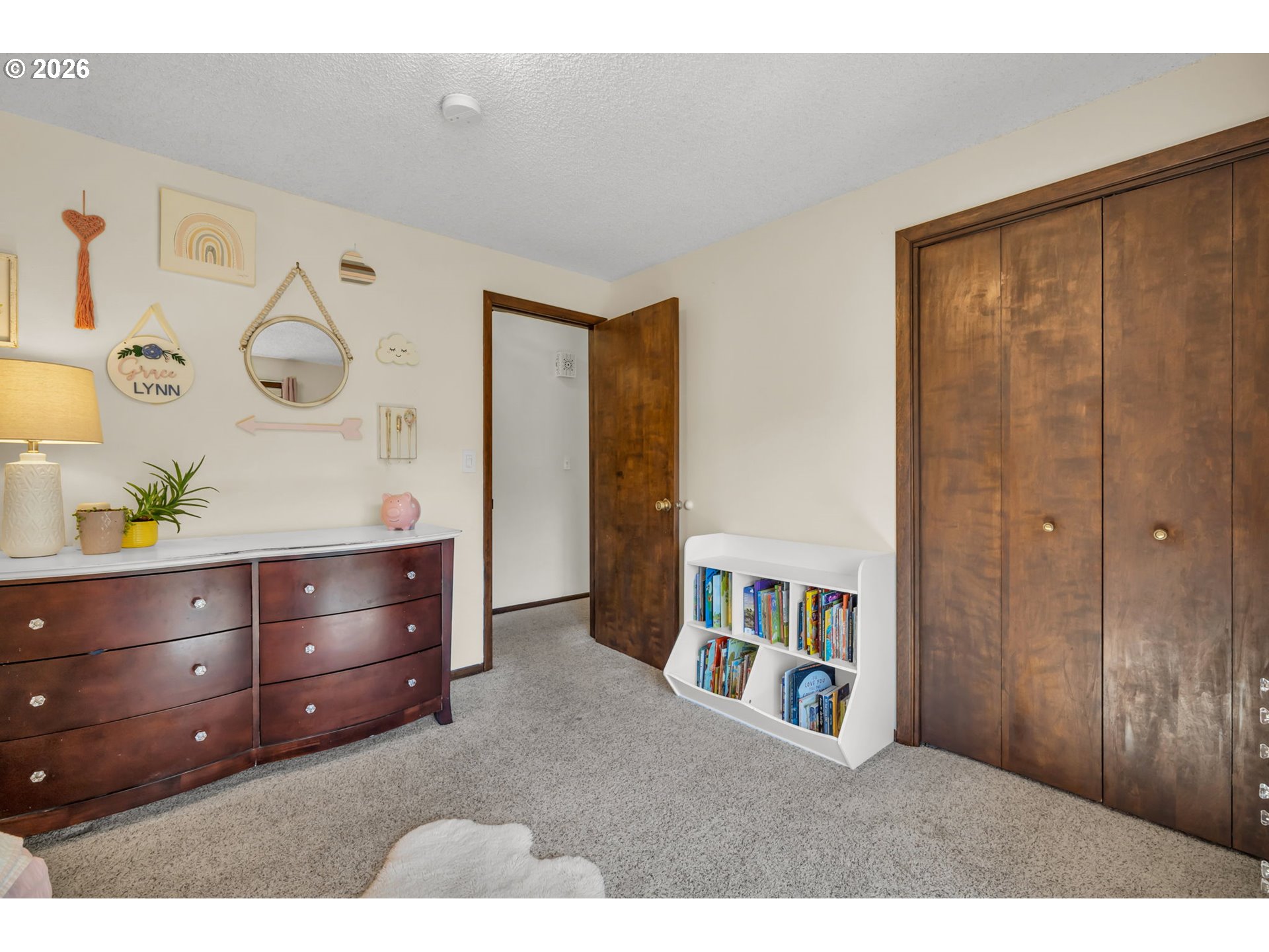 Bedroom with dark wood closet doors, a dresser, and a small bookshelf filled with children's books.