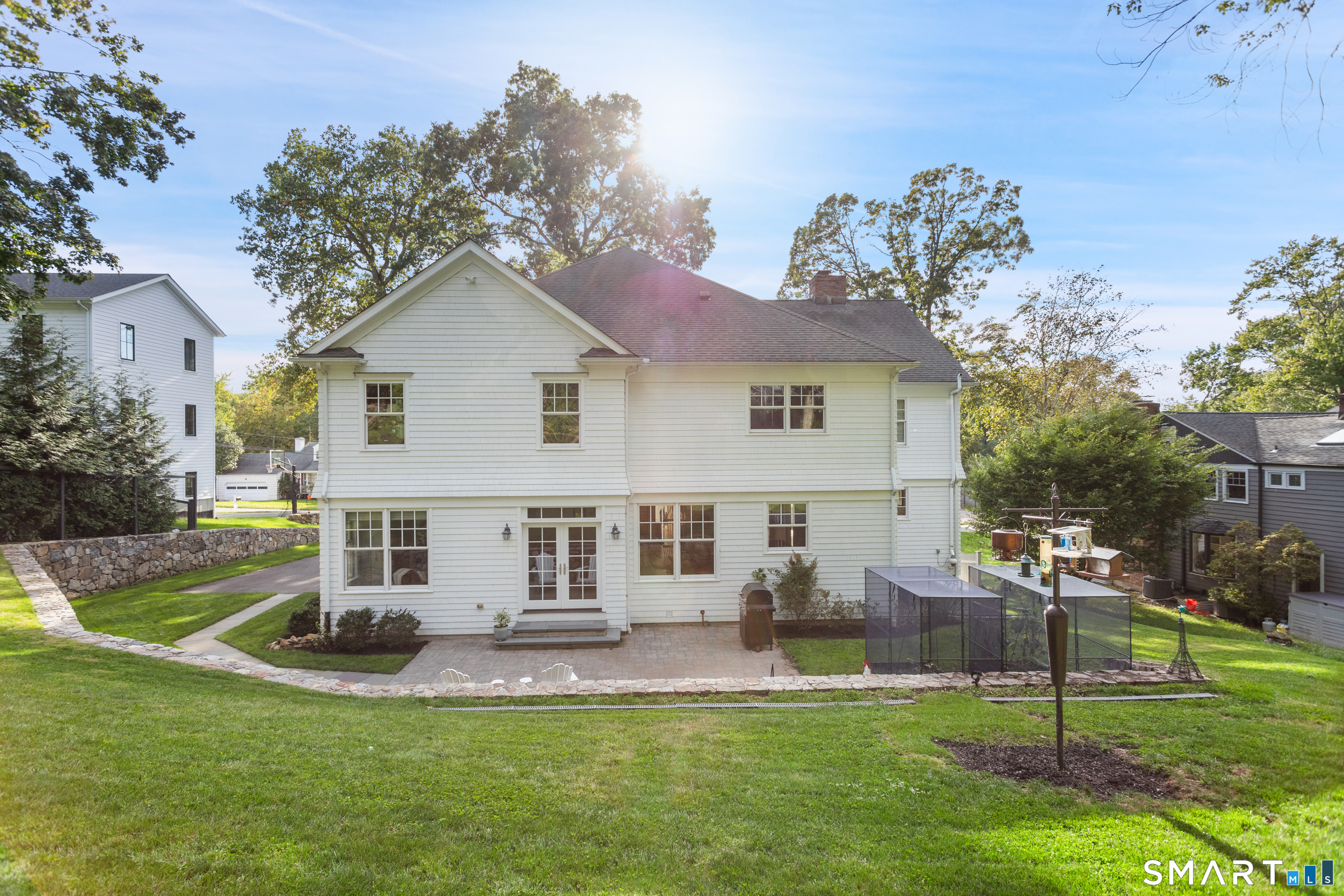 Rear of a white two-story house with a patio, fenced enclosure, and broad lawn.