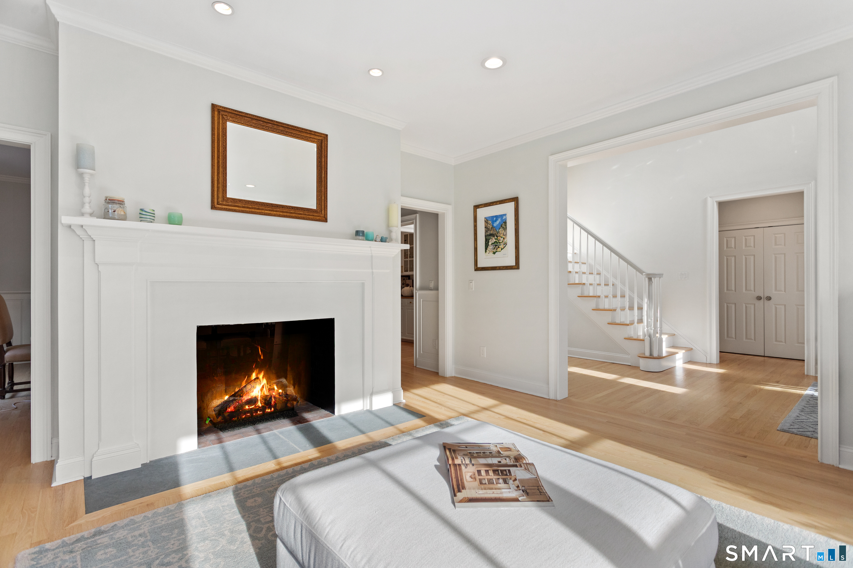 Bright living room with a lit fireplace, hardwood floors, and an open staircase.