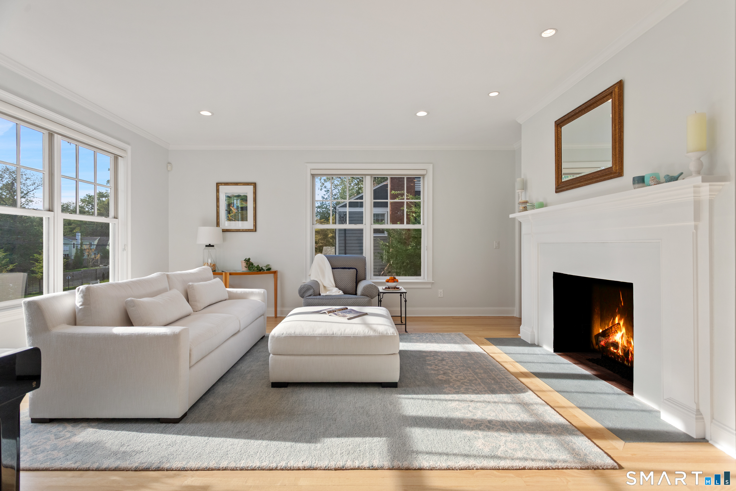 Furnished living room with a white sofa, large windows, and a lit fireplace.