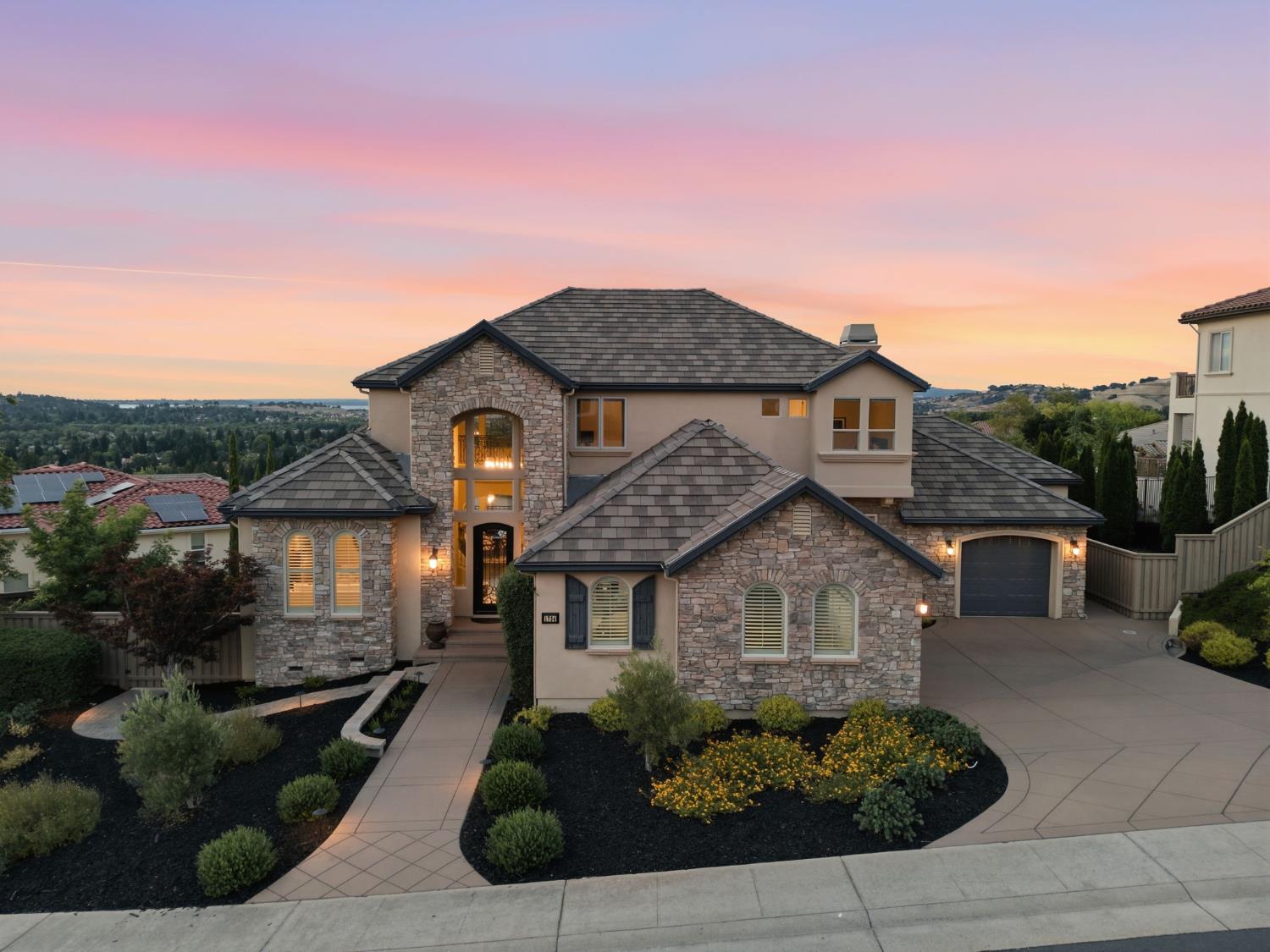 Stone-fronted two-story home with a landscaped entry and broad driveway at dusk.