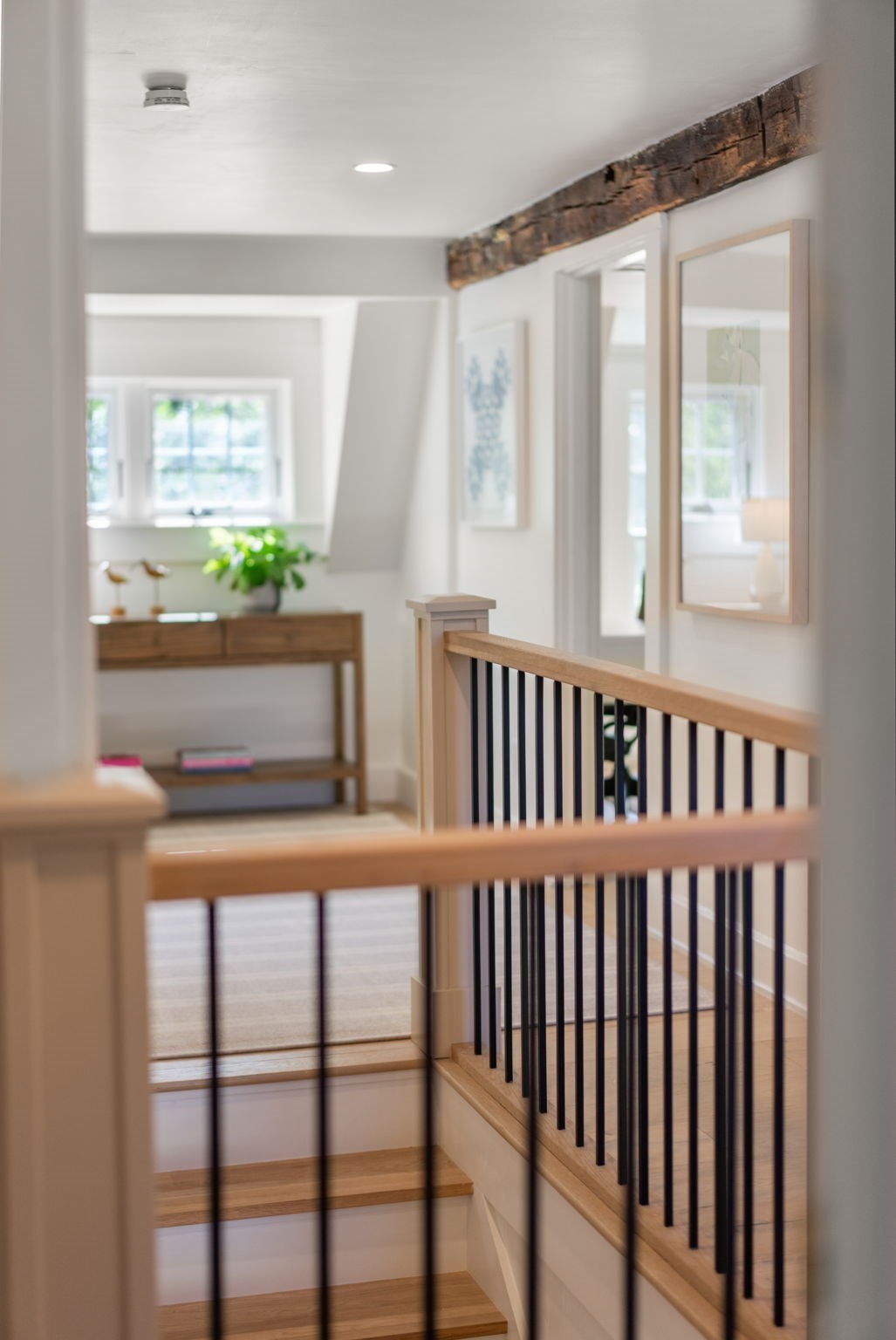 Bright hallway staircase with light wood railings, black balusters, and an exposed ceiling beam.