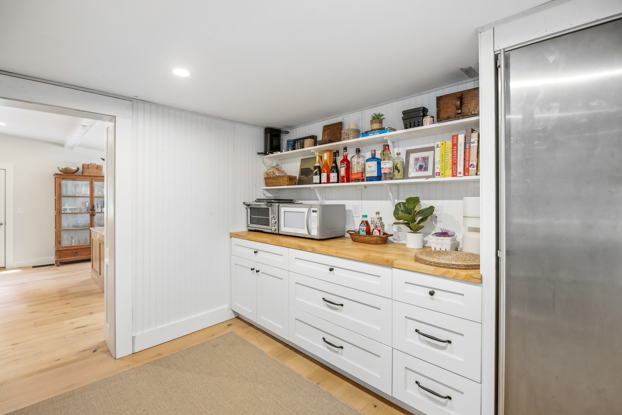 Kitchen pantry with white cabinets, open shelves, butcher-block counter, and stainless steel refrigerator.