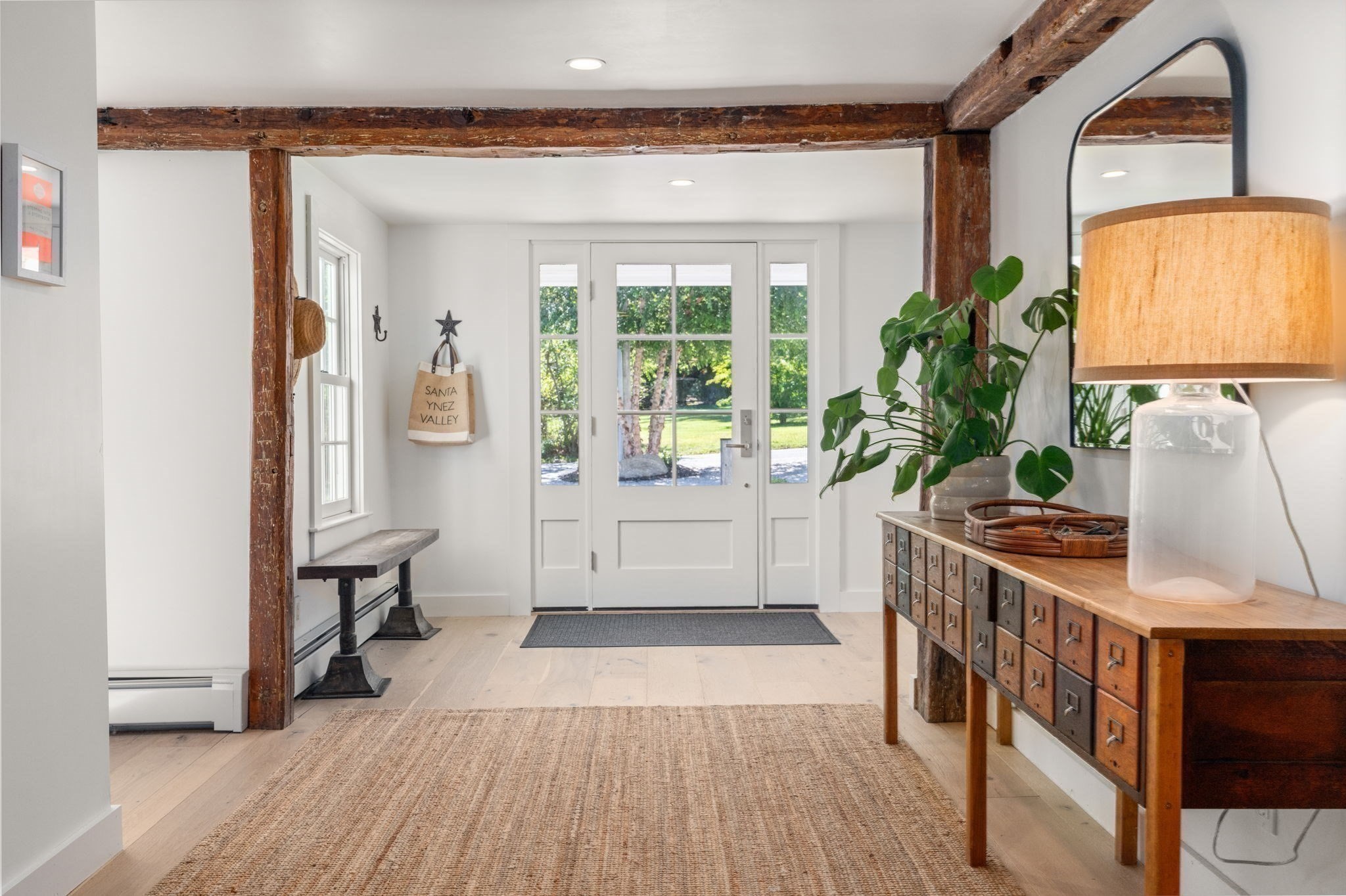 Bright entryway with exposed timber beams, a glass-paneled front door, and a wooden console.