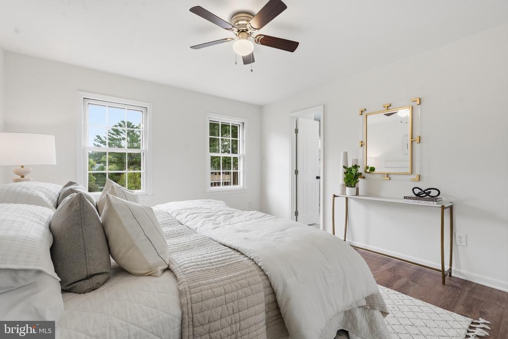 Bright staged bedroom with a white bed, two windows, and a ceiling fan.