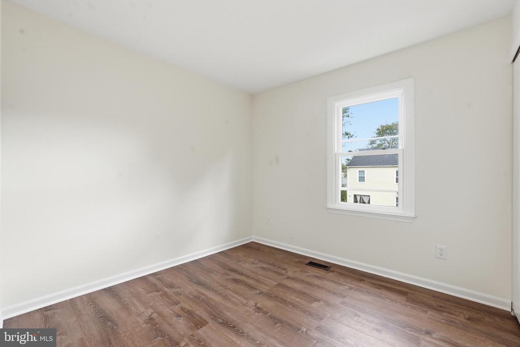 Empty bedroom with brown plank flooring and a single window overlooking a neighboring house.