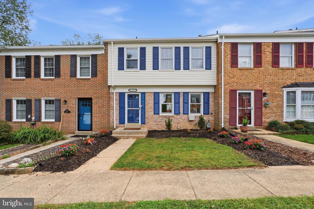 Brick townhouse with a cream-sided upper story, blue shutters and door, and landscaped front yard.