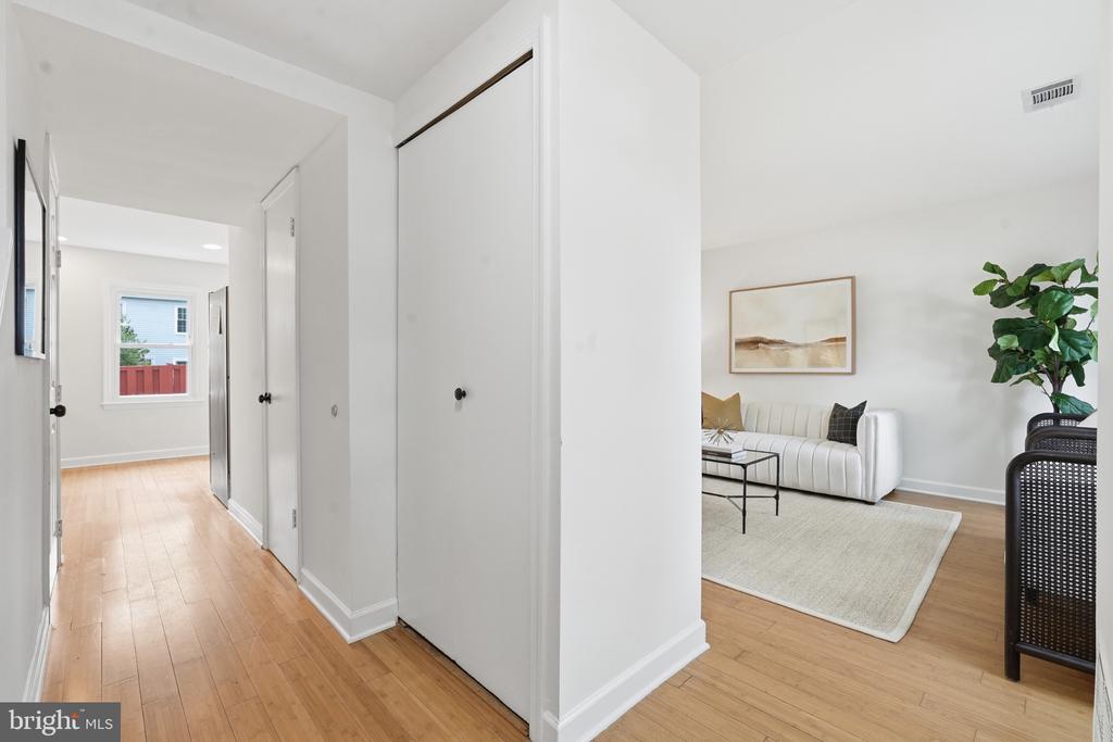 Hardwood hallway leading into a living room with a white sofa and large potted plant.