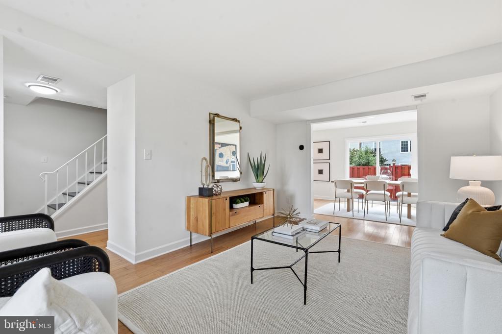 Staged living room with white sofas and a glass coffee table, opening into a dining area.