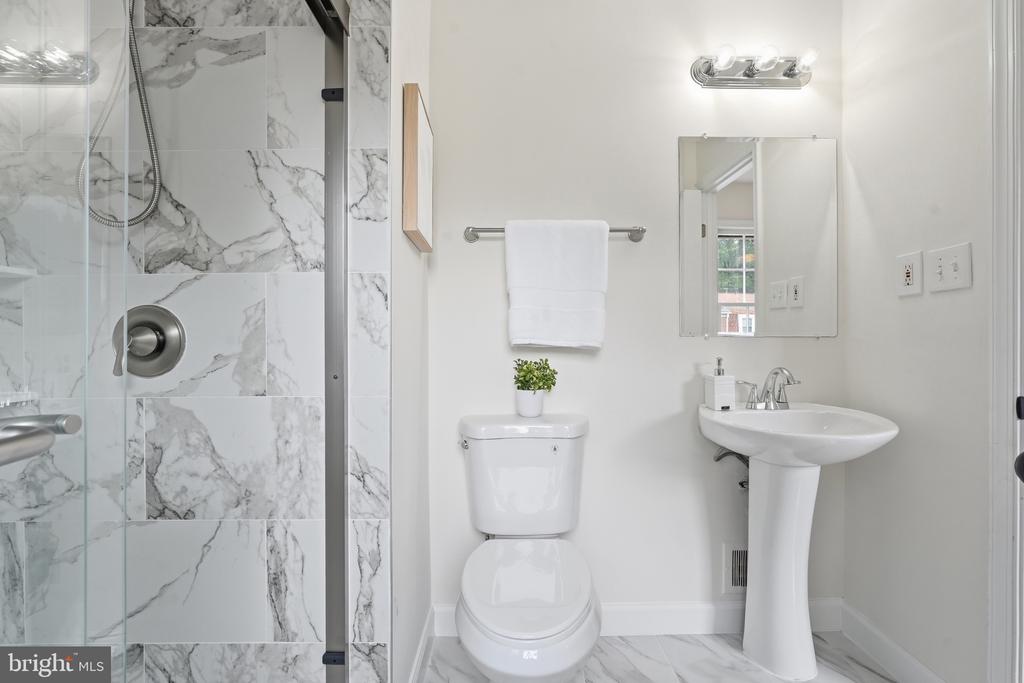 Bathroom with a marble-look tiled glass shower, white toilet, and pedestal sink.
