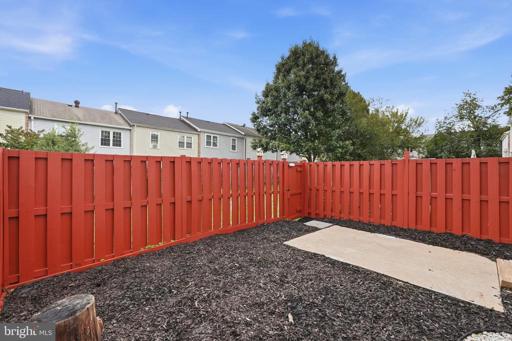 Backyard with a red privacy fence, mulched ground, and a concrete patio.