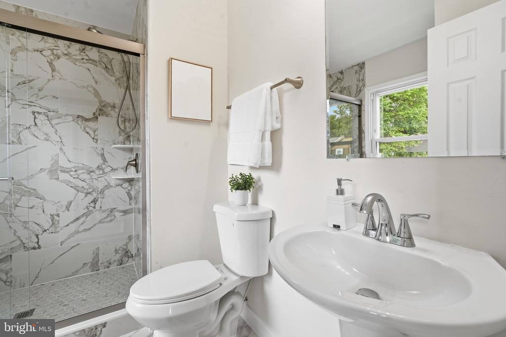 Bathroom with a glass-enclosed marble-look tile shower, white toilet, and sink vanity.