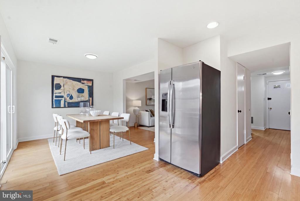 Dining area with a wood table and white chairs beside a stainless steel refrigerator.
