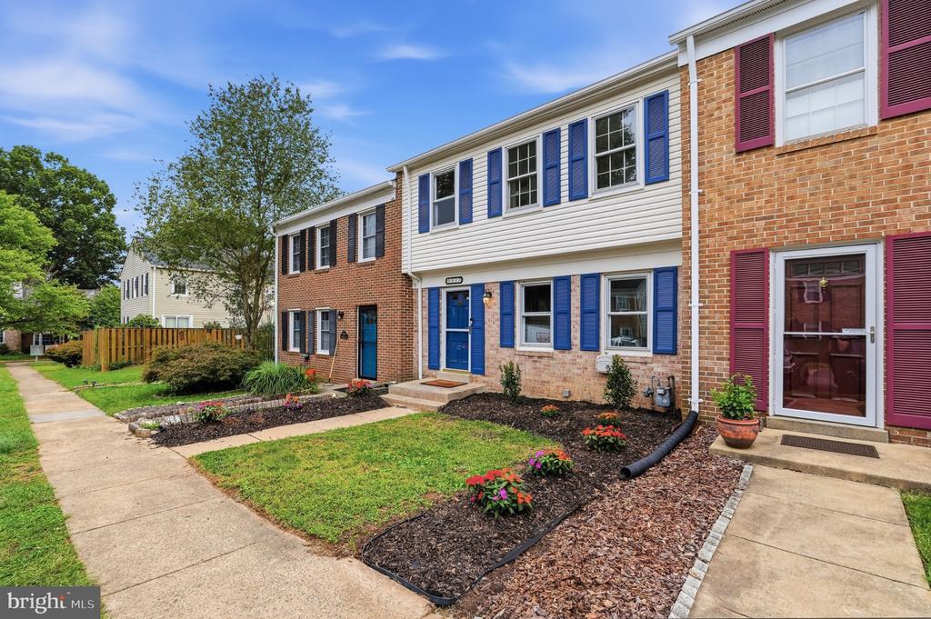 Brick townhome with white siding, blue shutters, and a landscaped front yard.