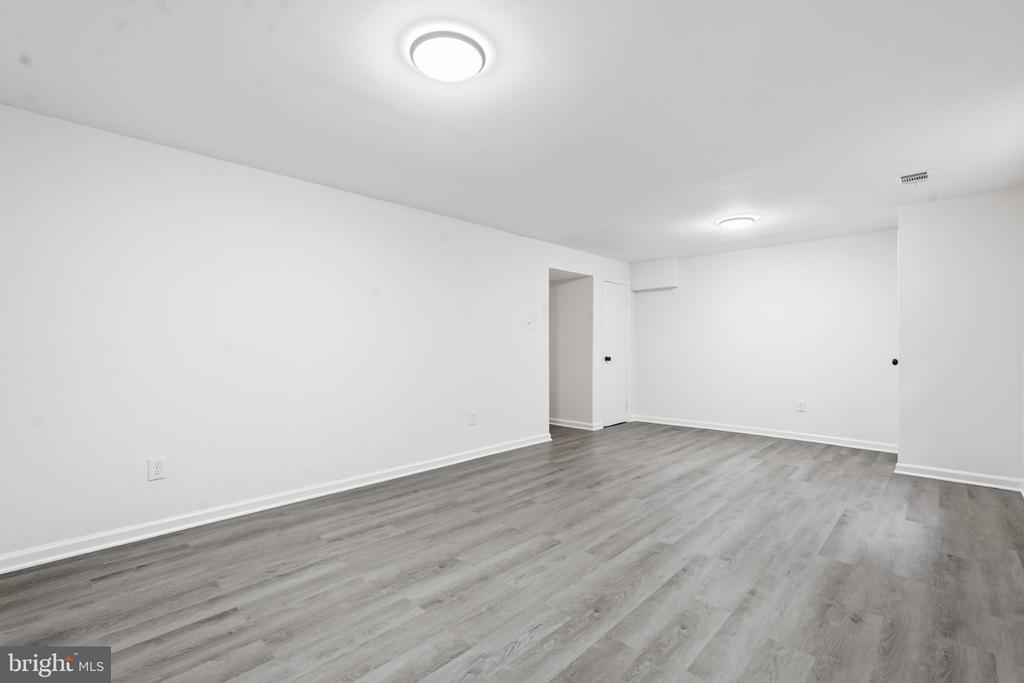 Empty finished room with gray plank flooring, white walls, and recessed ceiling lights.