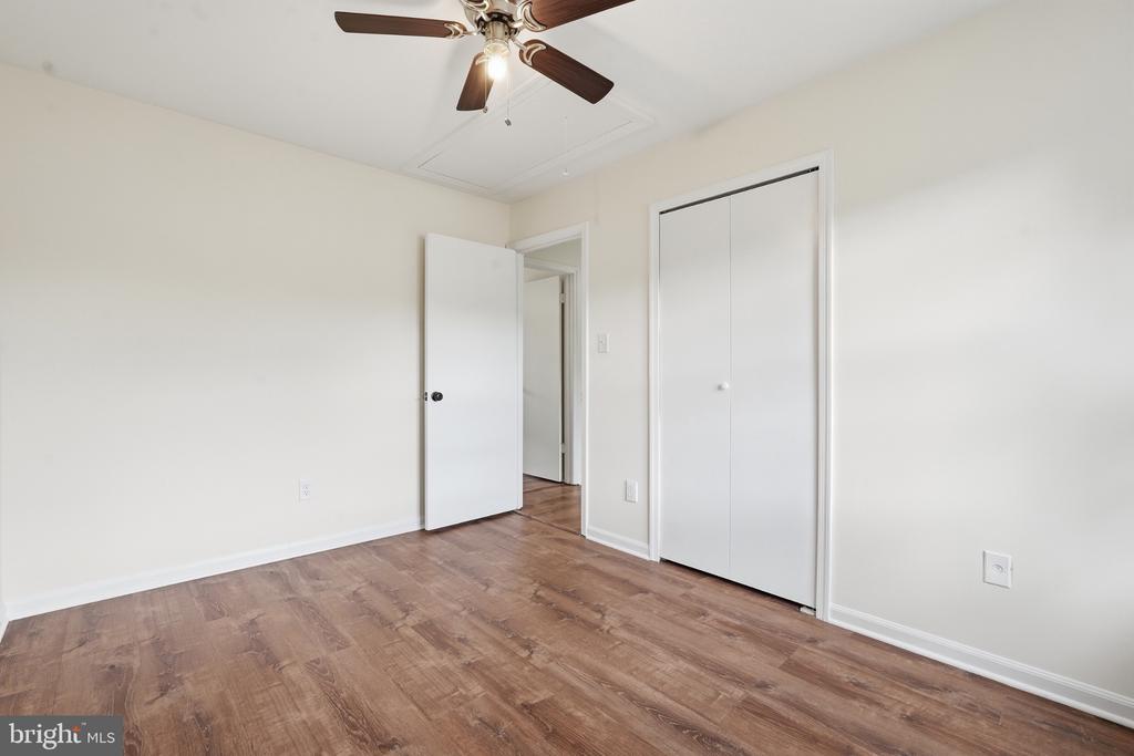 Empty bedroom with brown wood-look floors, a ceiling fan, and a double-door closet.