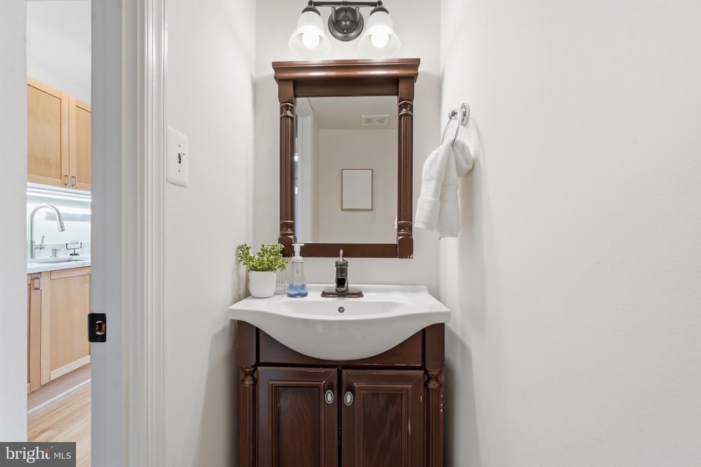Bathroom vanity with dark wood cabinetry, white sink, and framed mirror beside a kitchen doorway.