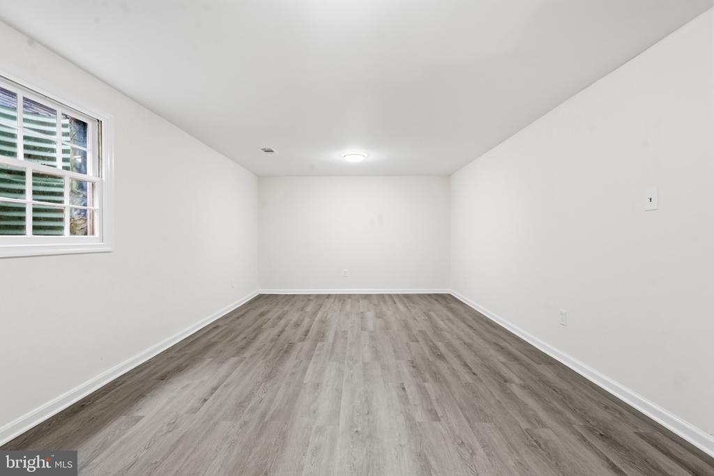 Empty room with gray plank flooring, white walls, and a shuttered window.