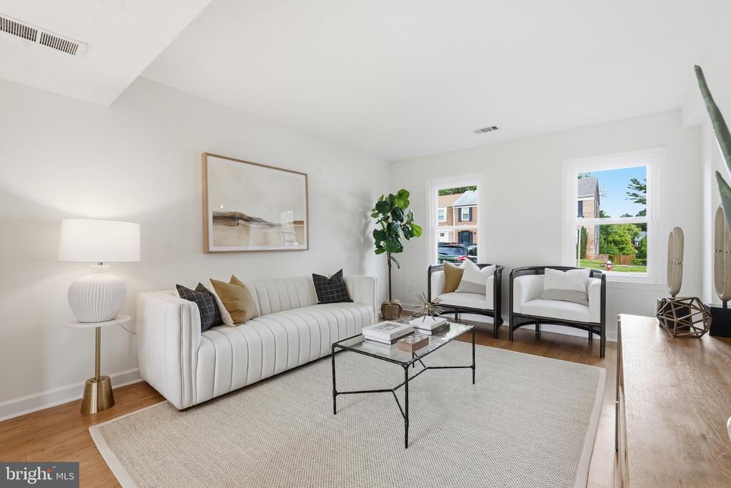 Staged living room with a white sofa, two armchairs, and large windows.